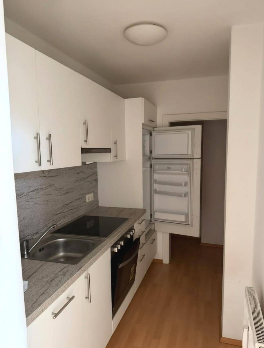 Funktionale Einbauküche mit weißen Schränken, Kochfeld und integriertem Kühlschrank.