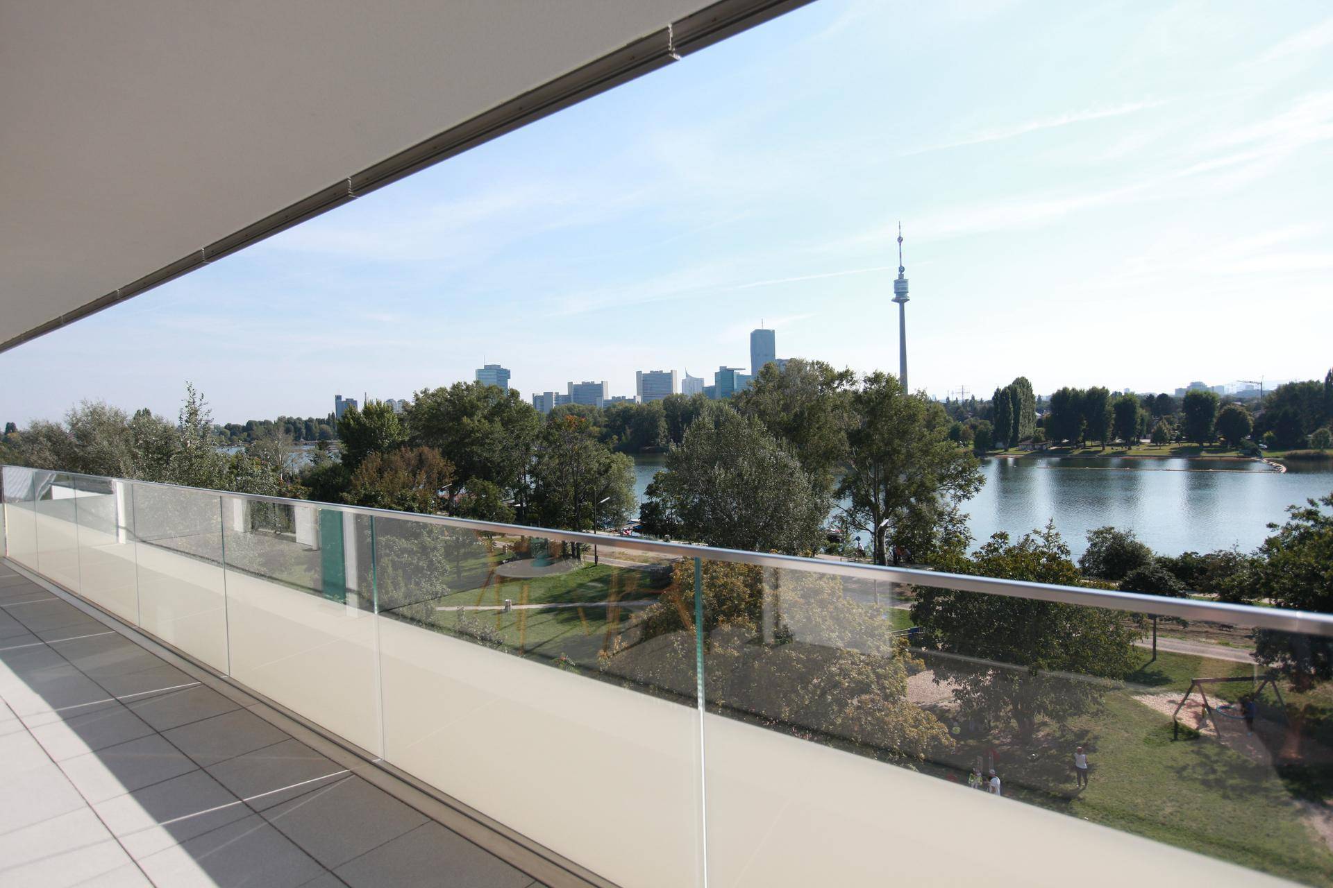 Geräumiger Balkon mit Glasgeländer und weitem Blick auf den See und die Stadt.
