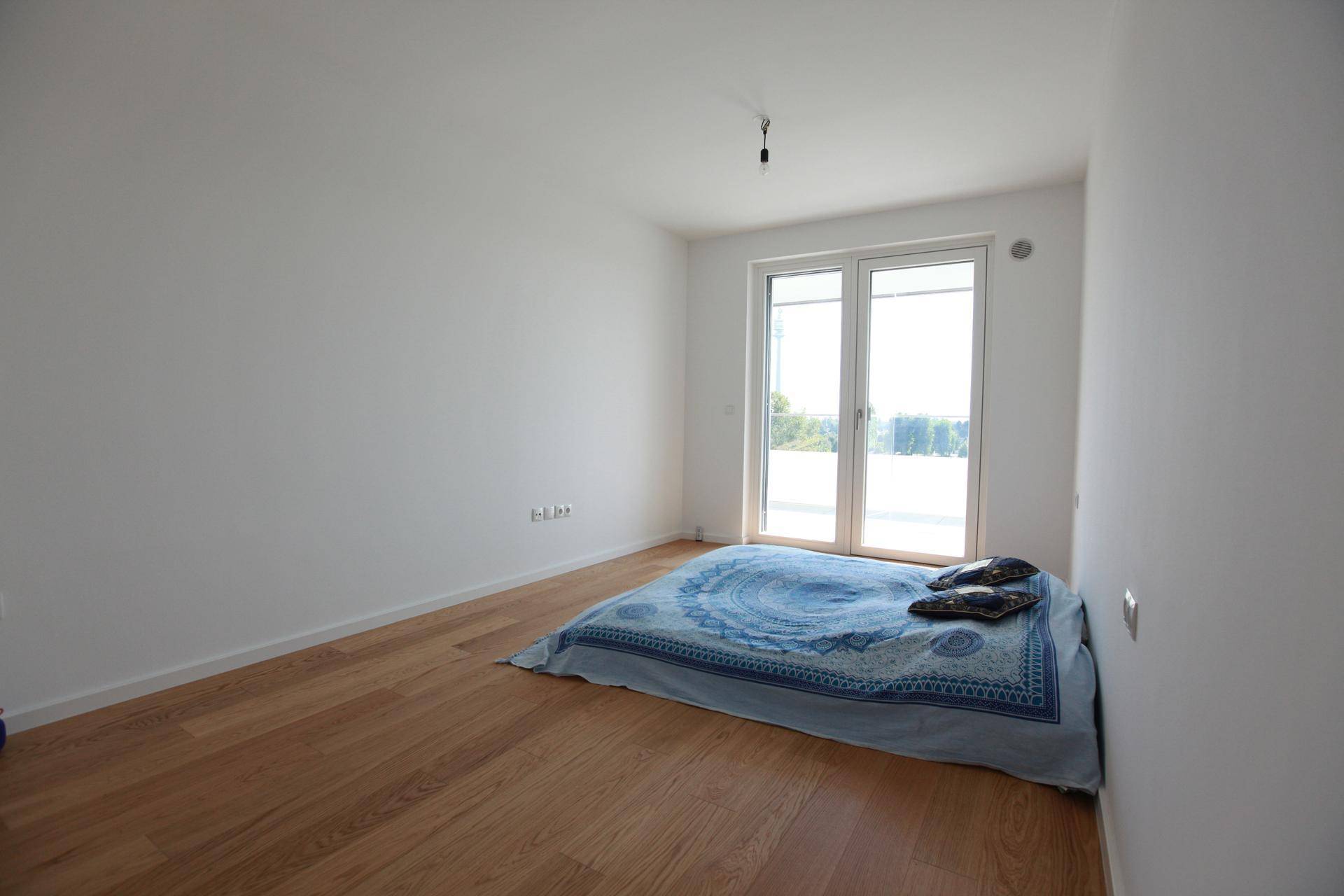 Schlafzimmer mit Holzboden und großen Fenstern, die viel Tageslicht hereinlassen.