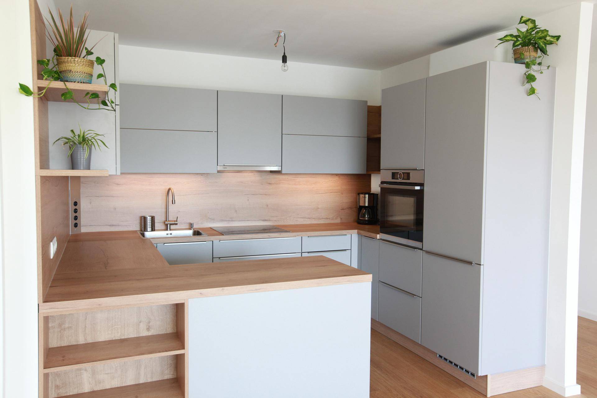 Moderne Einbauküche mit grauen Fronten, Holzdetails und integrierten Geräten.