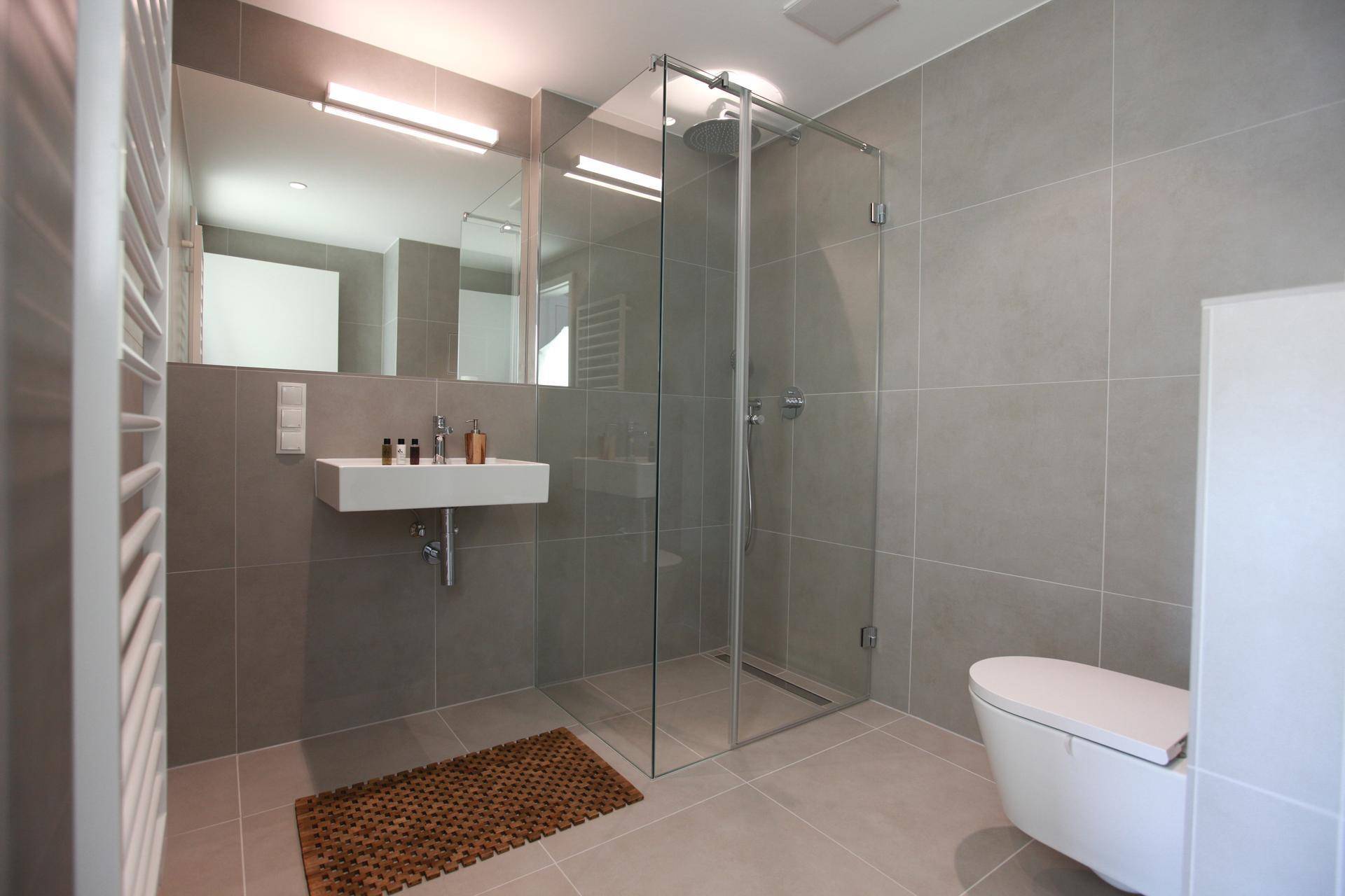 Zeitgemäßes Badezimmer mit ebenerdiger Dusche, Wand-WC und grauen Fliesen.