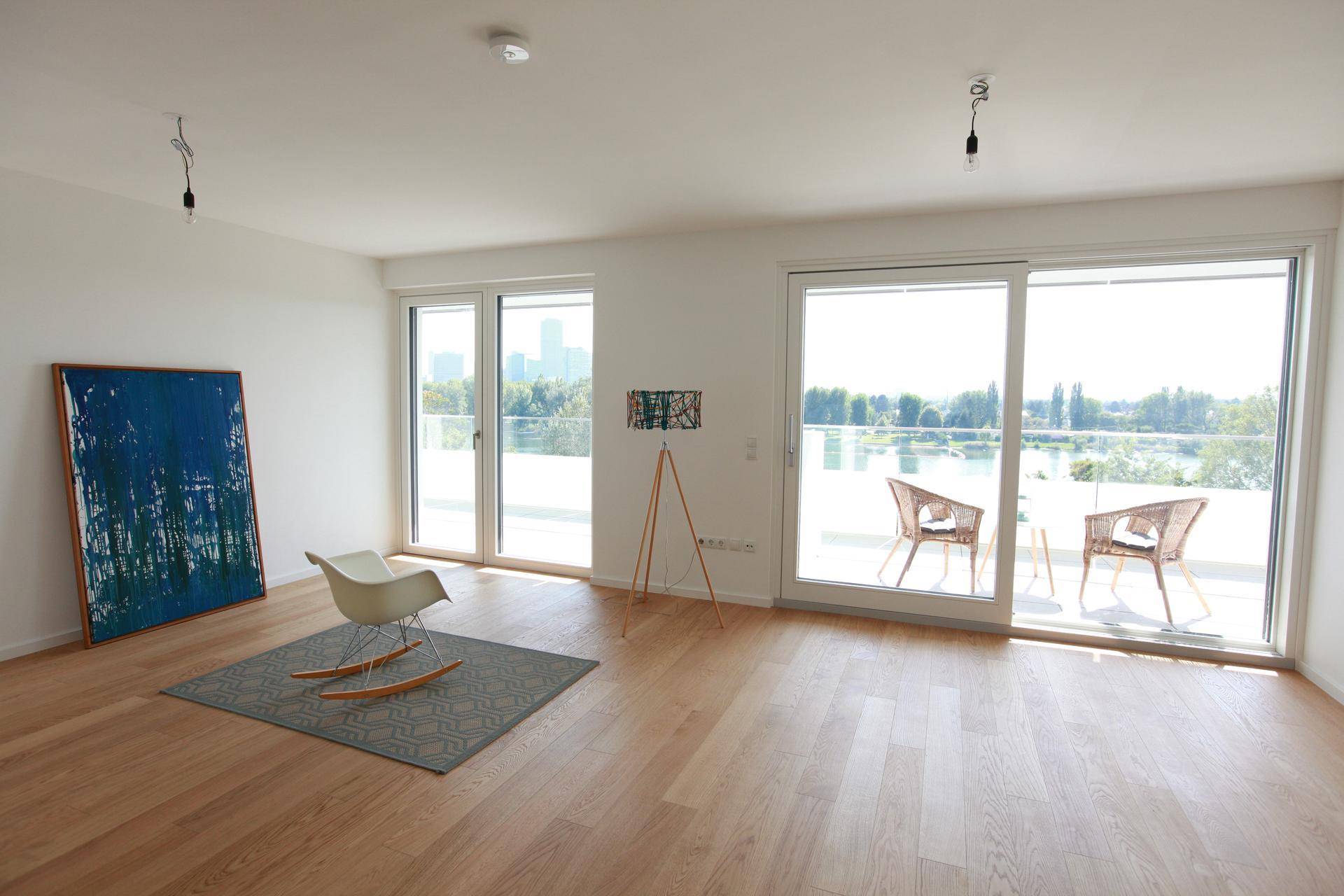 Helles Wohnzimmer mit Holzboden, großen Fenstern und Zugang zu einer Terrasse mit Seeblick.