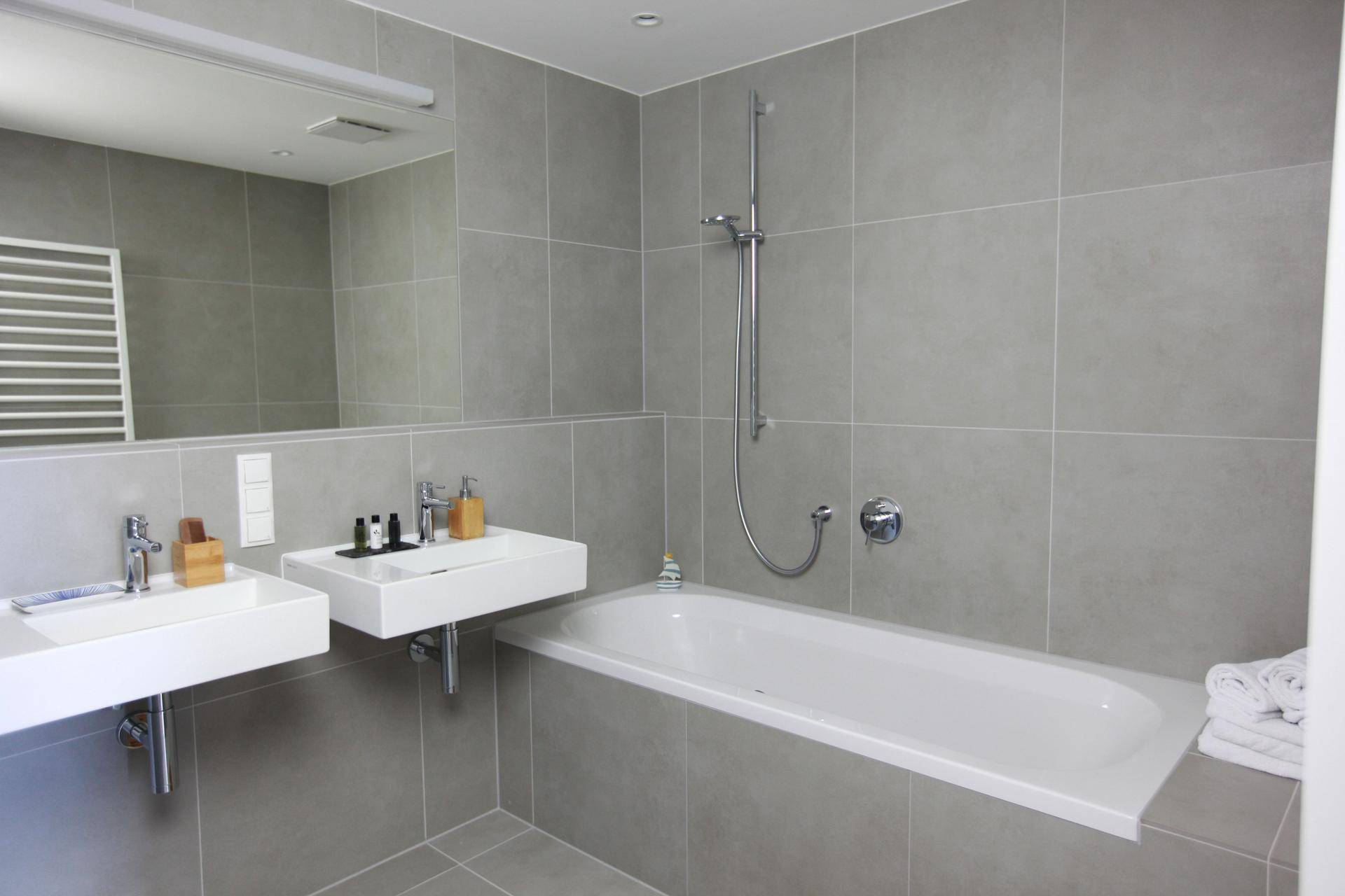 Modernes Badezimmer mit doppelten Waschbecken, Badewanne und grauen Fliesen.