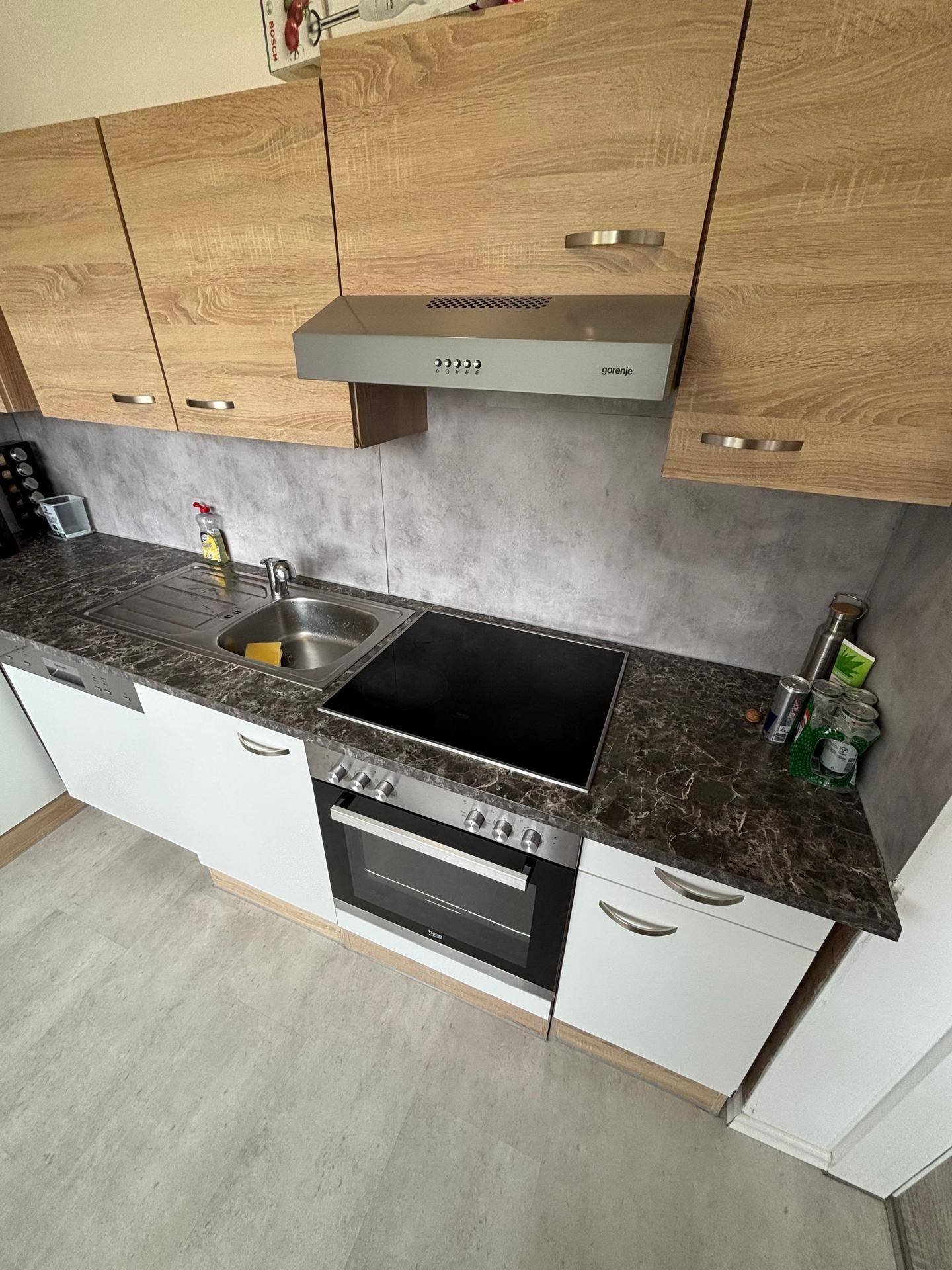 Küchenzeile mit Spüle, Cerankochfeld und Backofen, umgeben von Holz- und weißen Schränken.