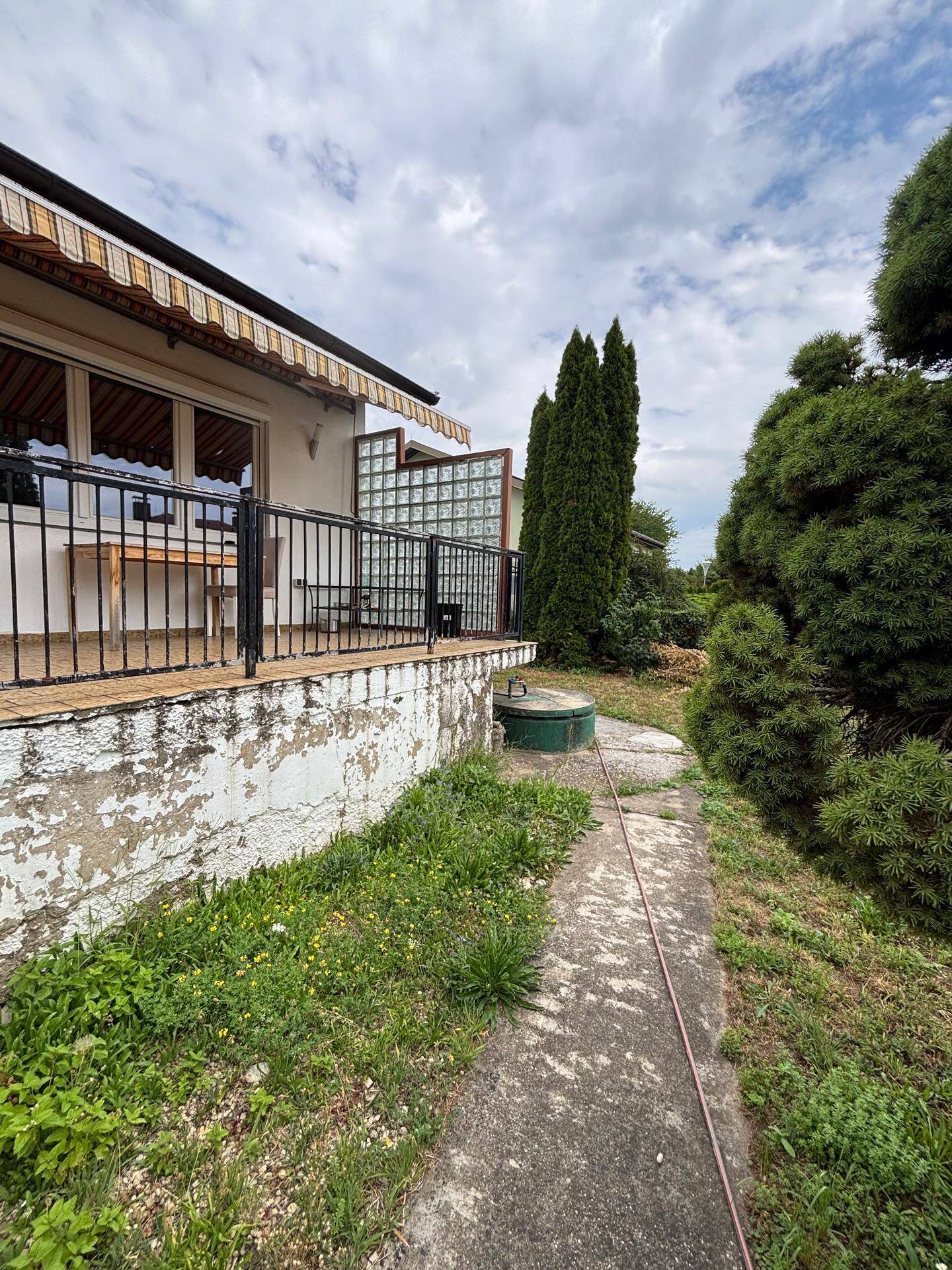 Seitenansicht des Hauses mit Gartenweg, Markise und einer Glasbausteinwand im Außenbereich.