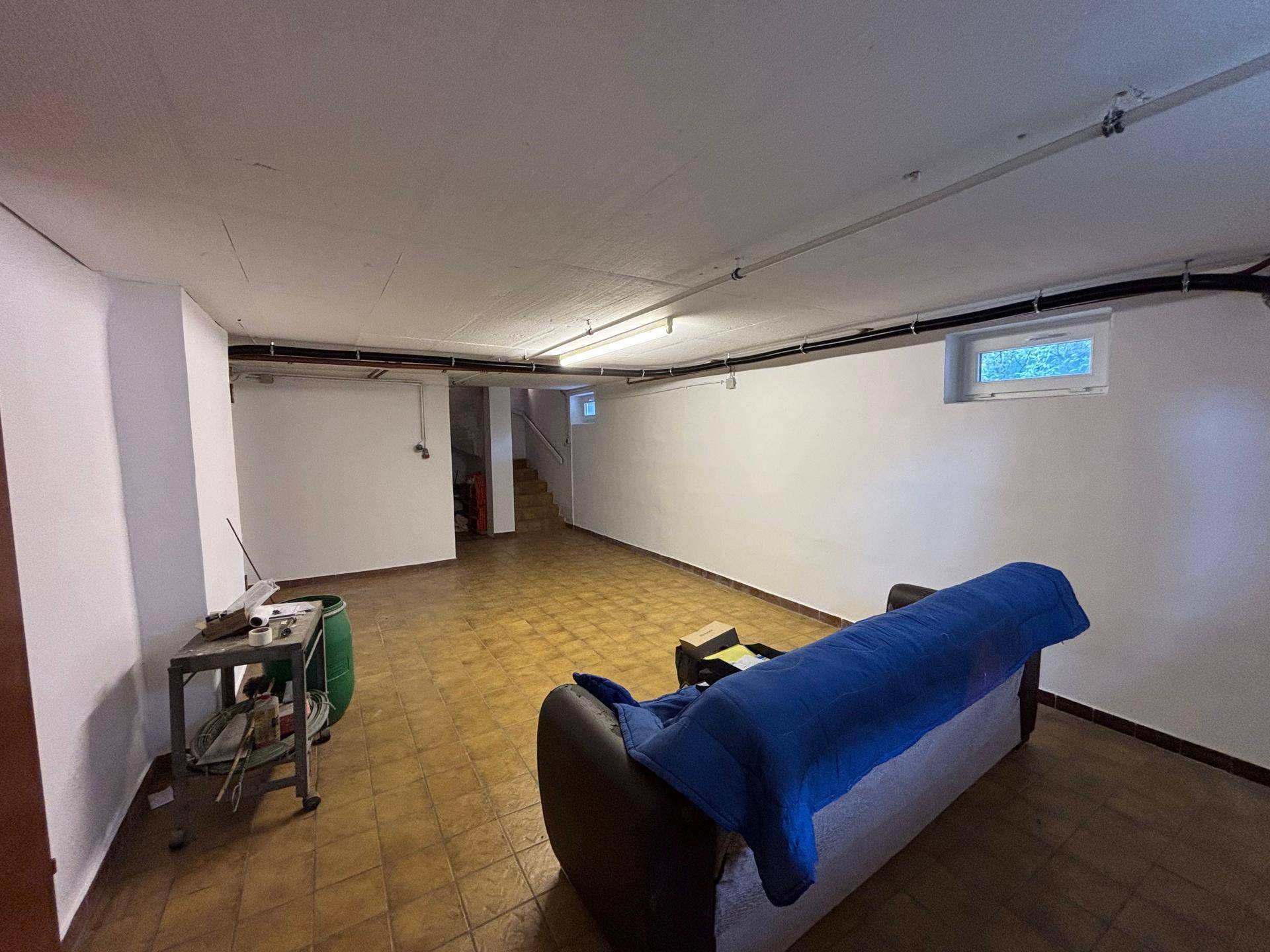Geräumiger Kellerraum mit Fliesenboden, Sofa und kleinem Fenster.