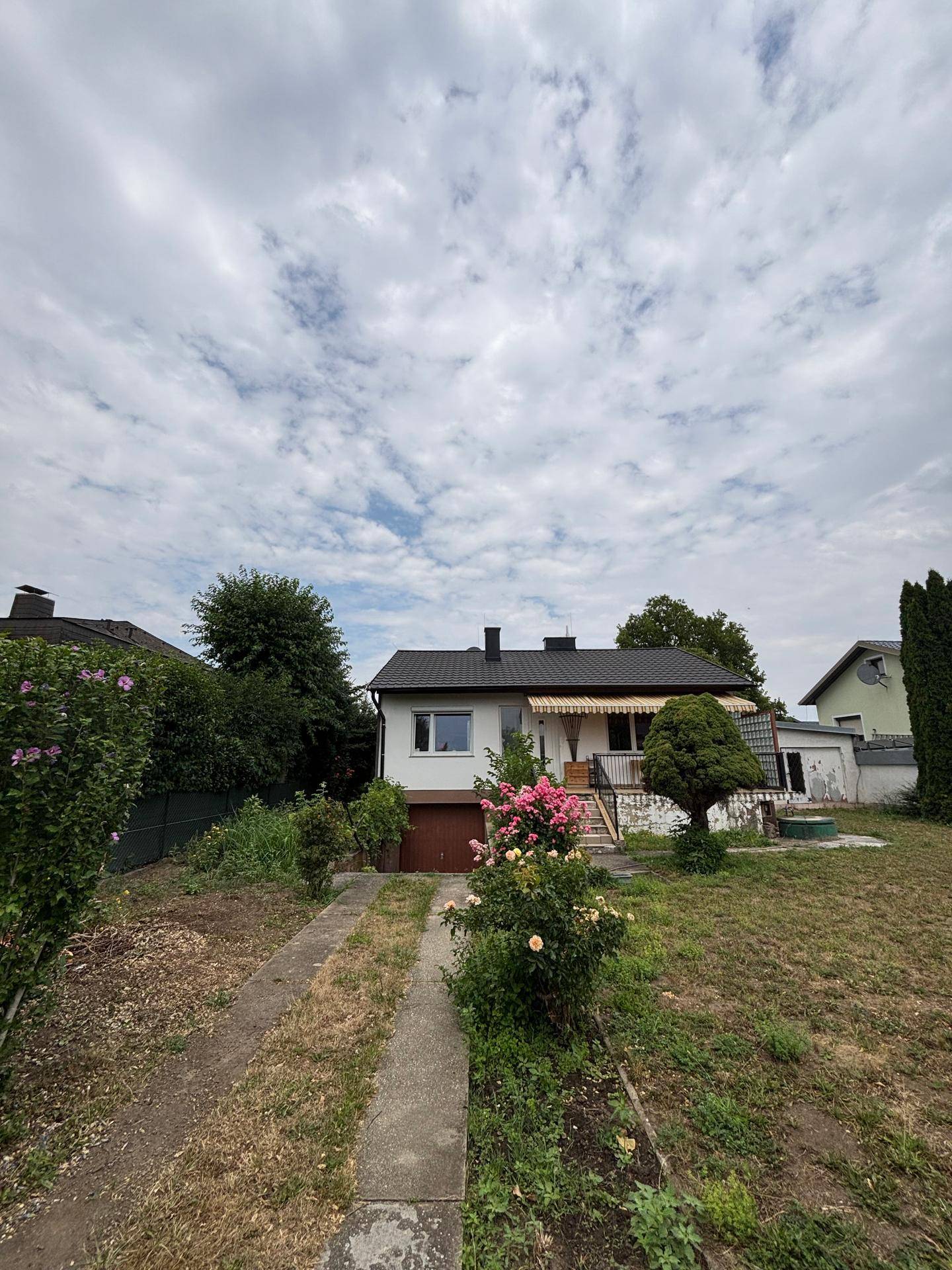 Einfamilienhaus mit Garage, Markise und einem ungepflegten Vorgarten mit Zufahrt.