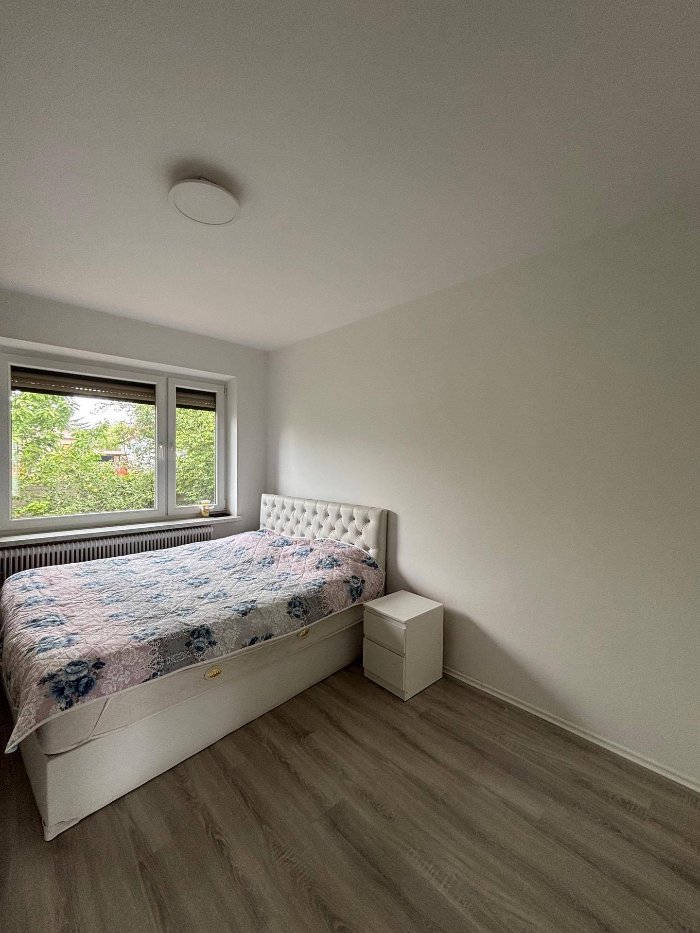 Helles Schlafzimmer mit Einzelbett, Nachttisch und Fenster mit Blick ins Grüne.