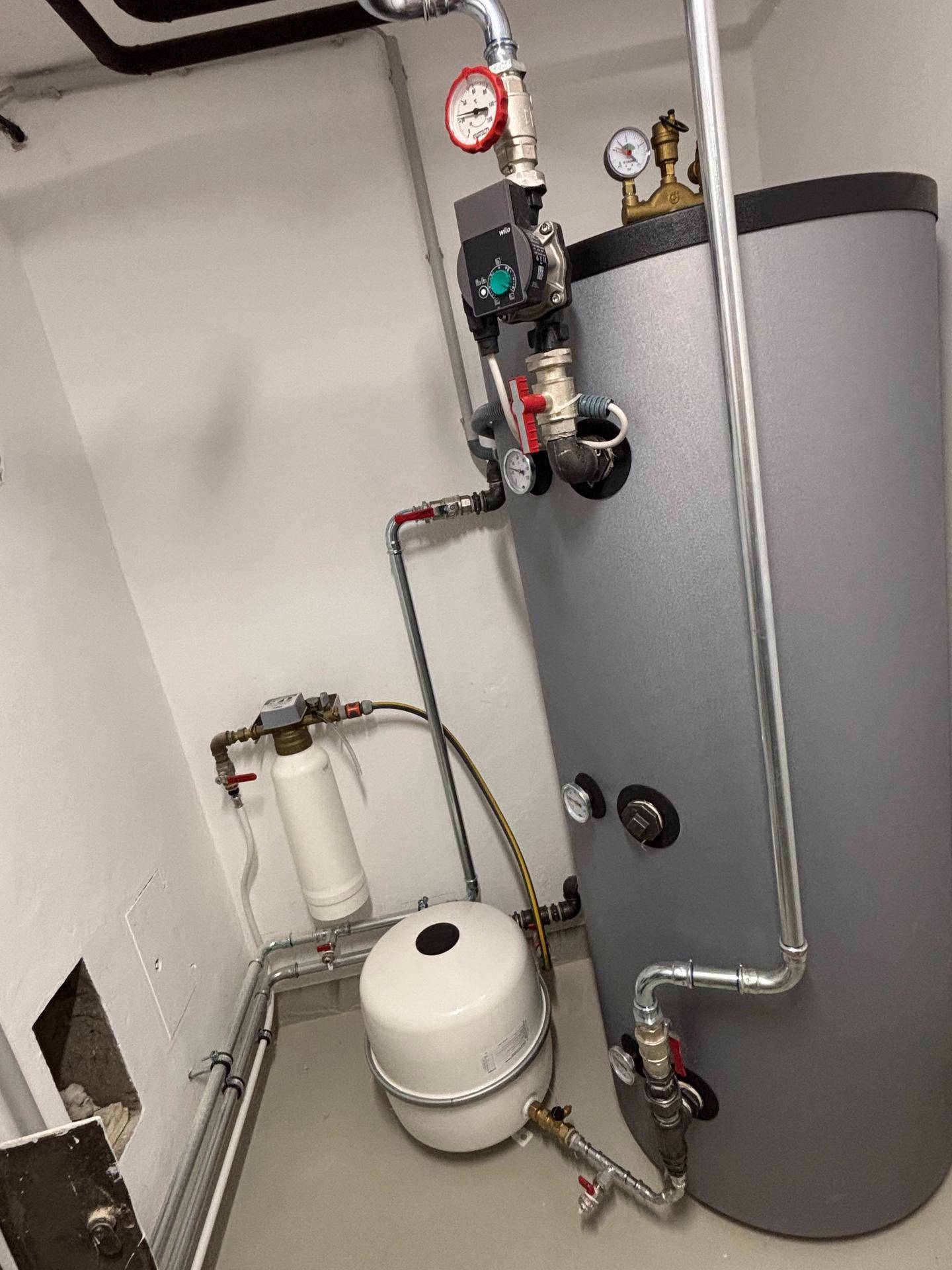 Heizungsraum mit Warmwasserspeicher und sichtbaren Rohrleitungen.