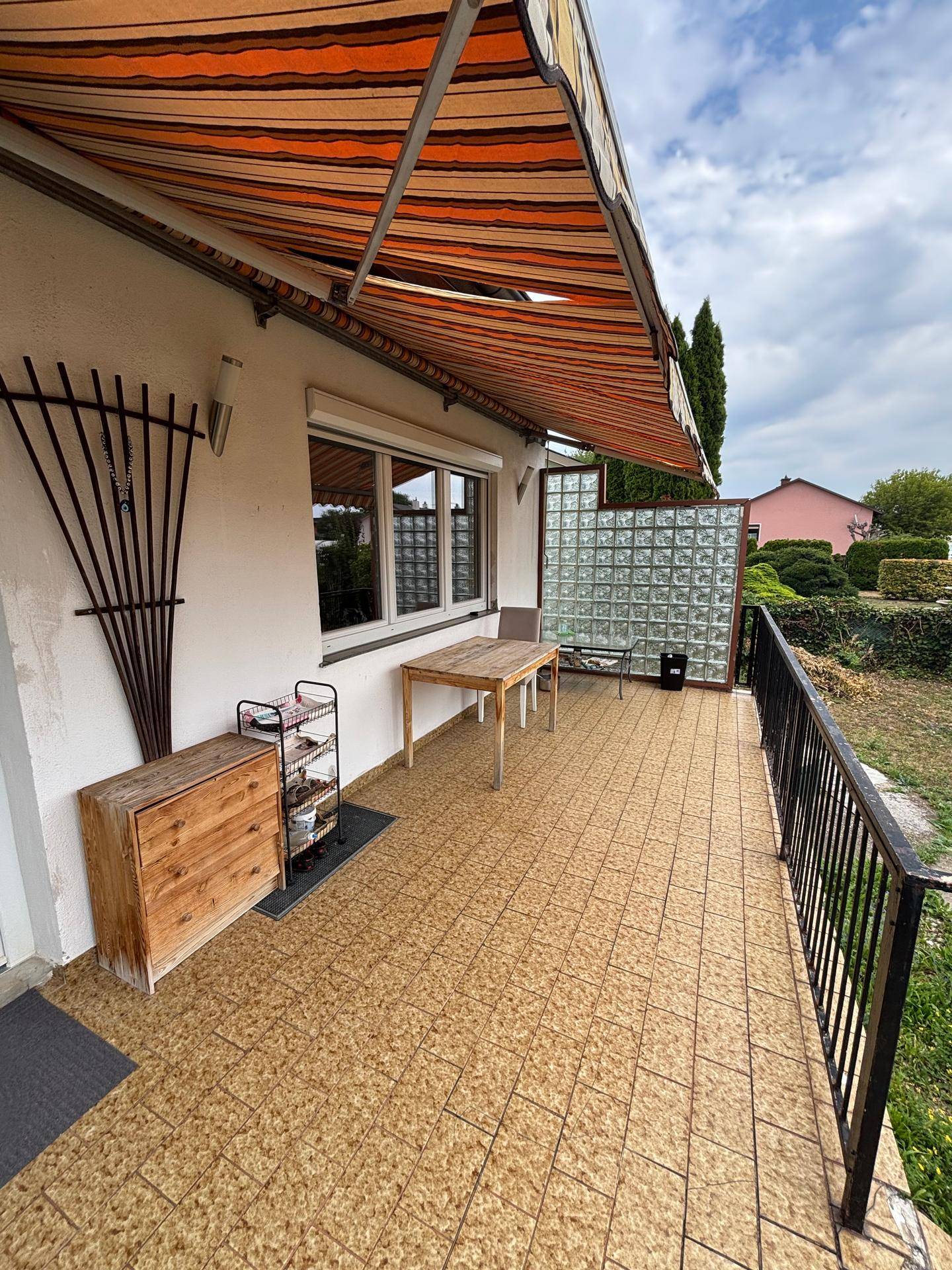 Gemütliche Terrasse mit Markise, Glastrennwand und einem kleinen Holztisch für entspannte Stunden.