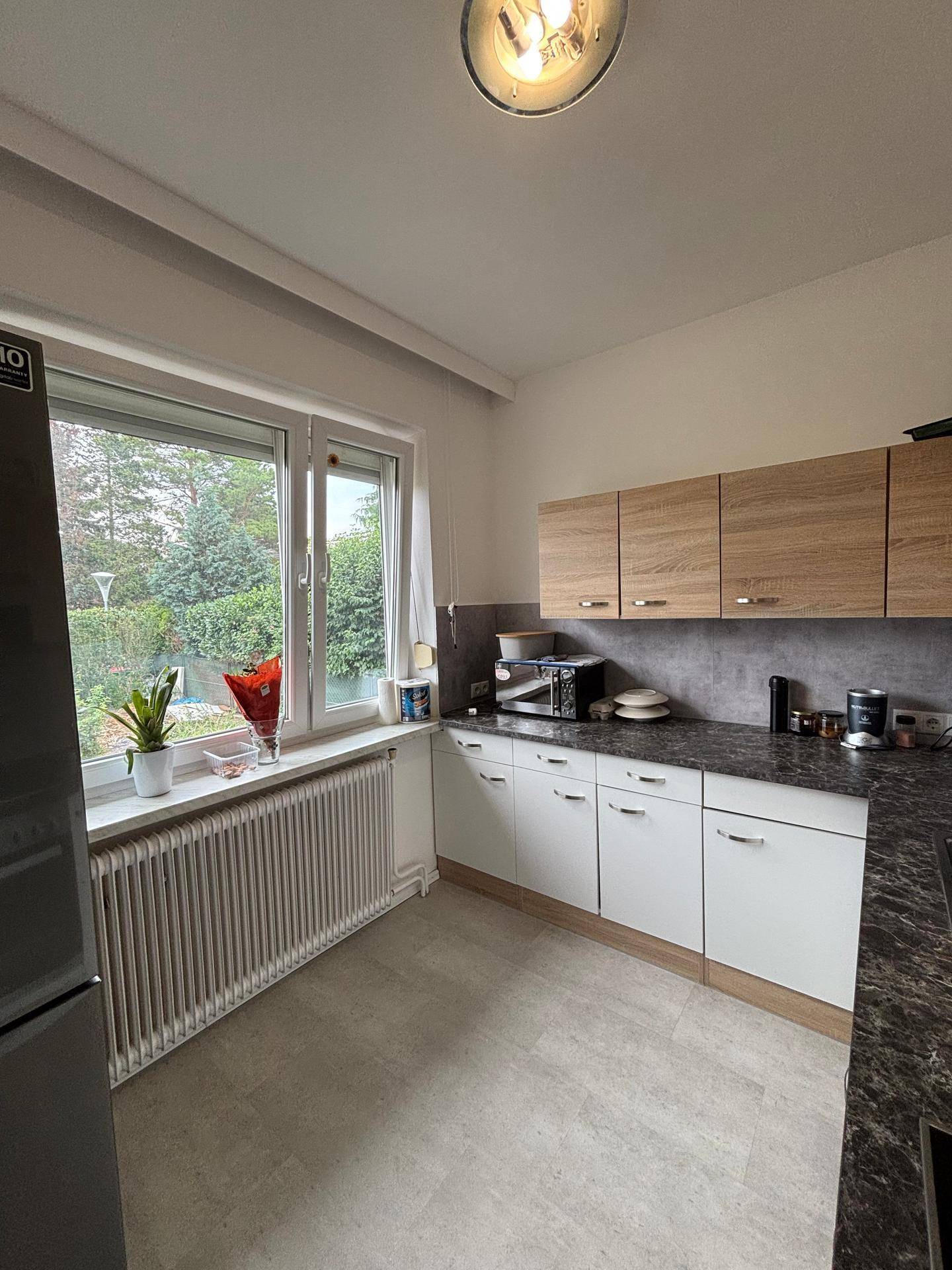 Helle Küche mit Fenster, Holz- und weißen Schränken sowie einem Heizkörper unter dem Fenster.