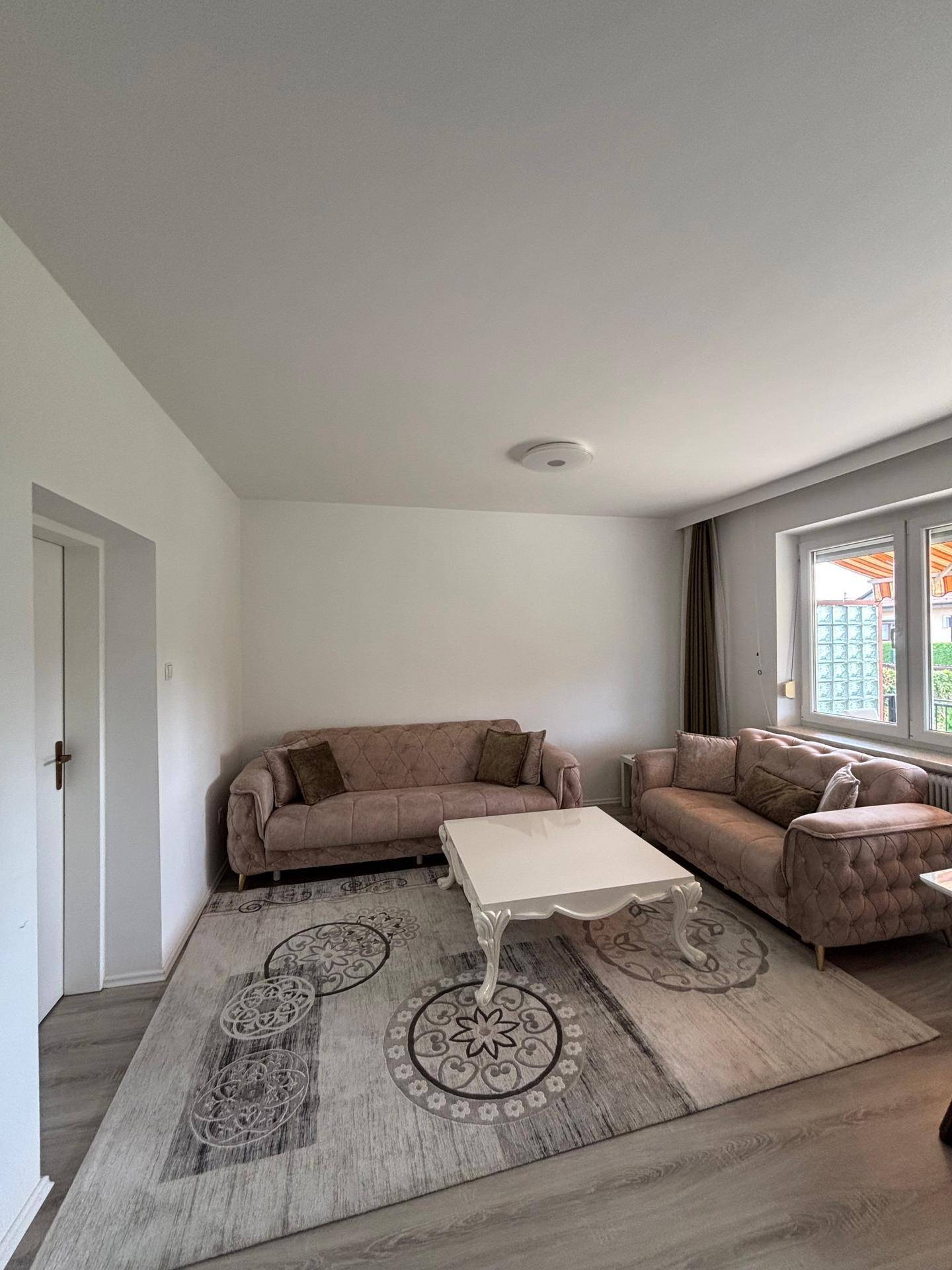 Geräumiges Wohnzimmer mit zwei beigen Sofas, einem Couchtisch und einem gemusterten Teppich.