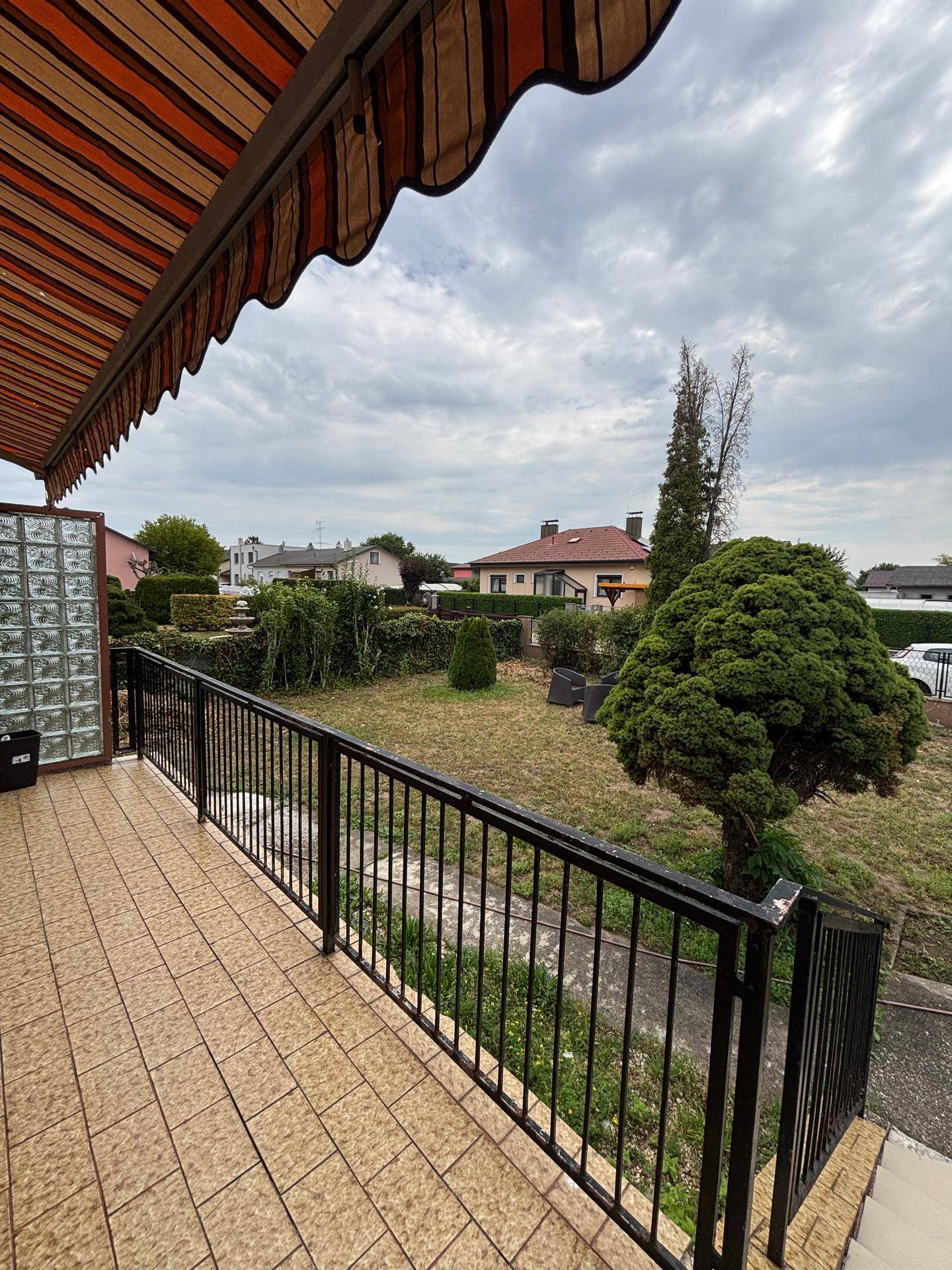 Geflieste Terrasse mit Markise und Blick auf den Garten und die Nachbarschaft.