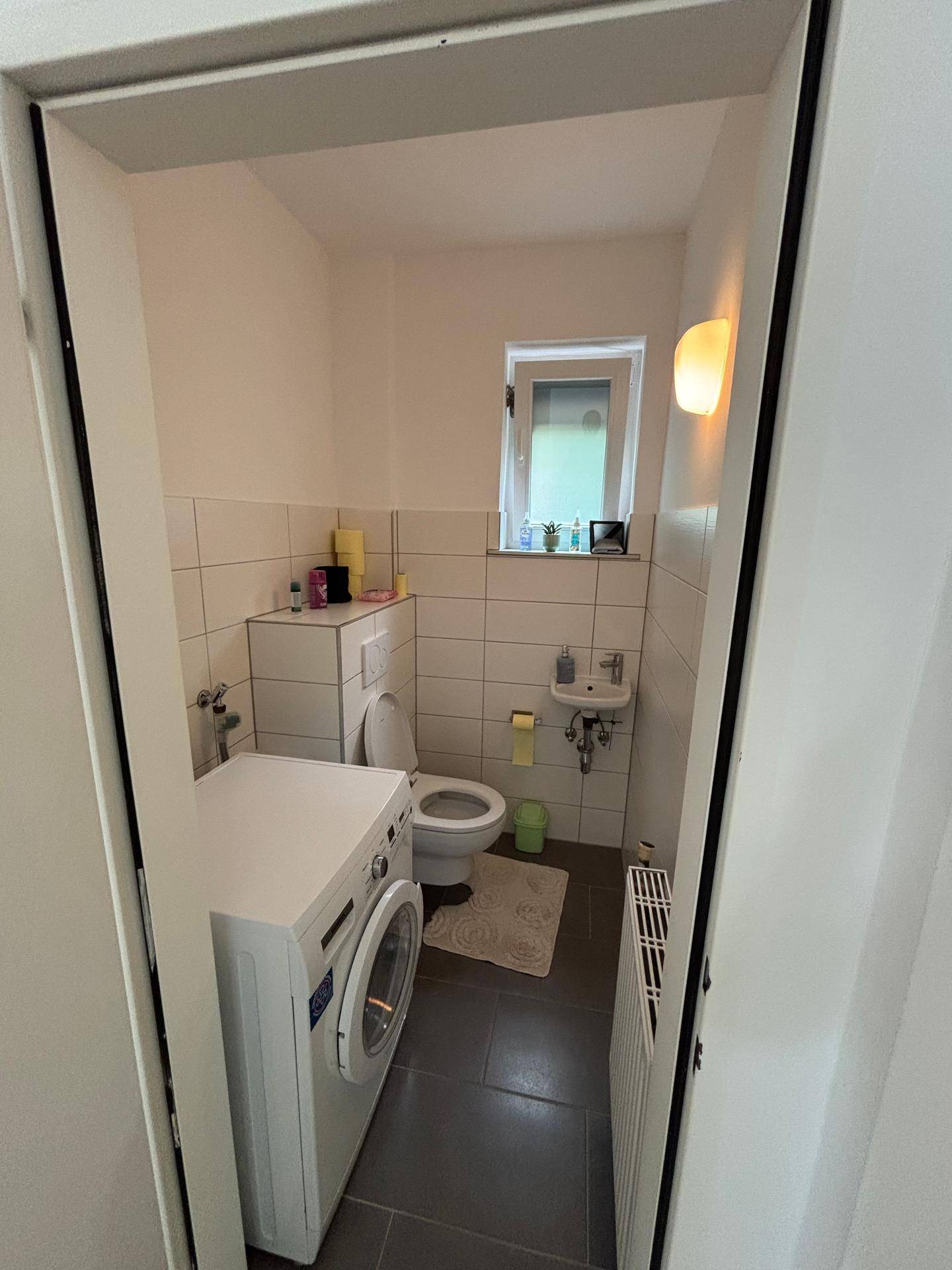 Separates WC mit Waschmaschine, Toilette und kleinem Waschbecken.