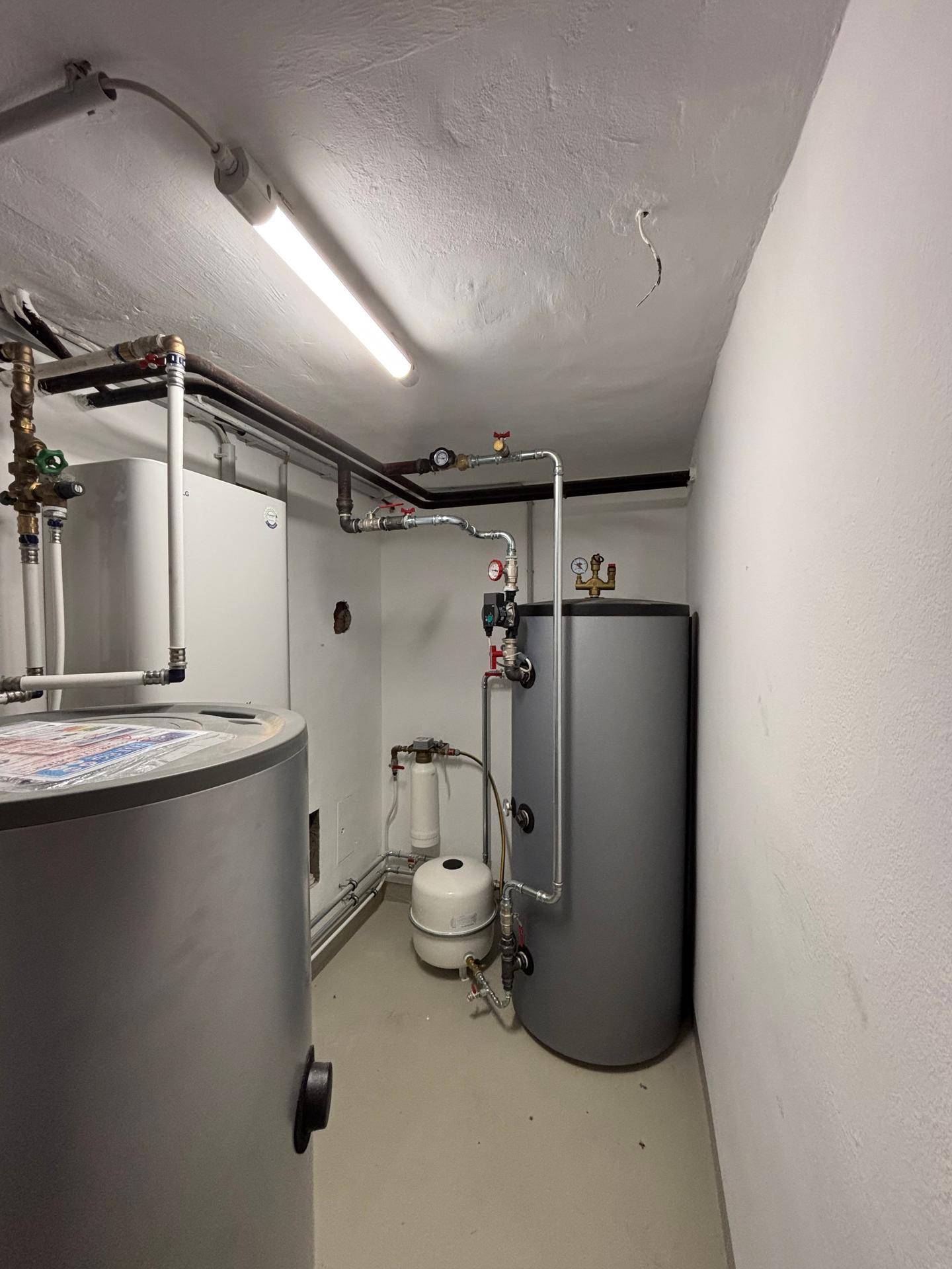 Geräumiger Hauswirtschaftsraum mit Heizungsanlagen, Wassertanks und sichtbaren Rohrleitungen.