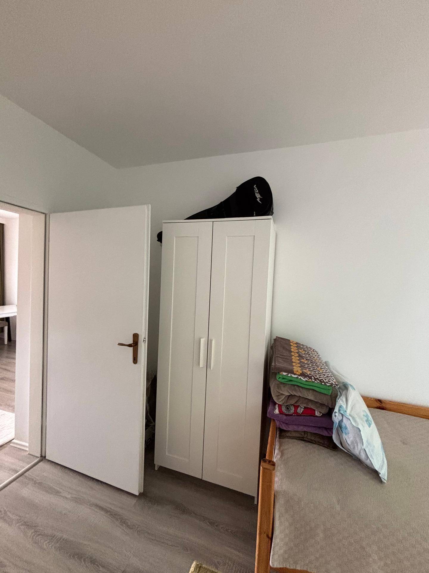 Schlafzimmer mit weißem Kleiderschrank und einem einfachen Bett, bereit zur individuellen Gestaltung.
