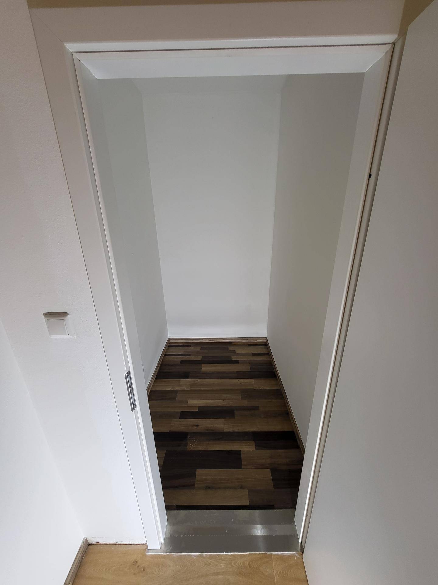 Schmaler Abstellraum mit dunklem Laminatboden, ideal für zusätzlichen Stauraum.