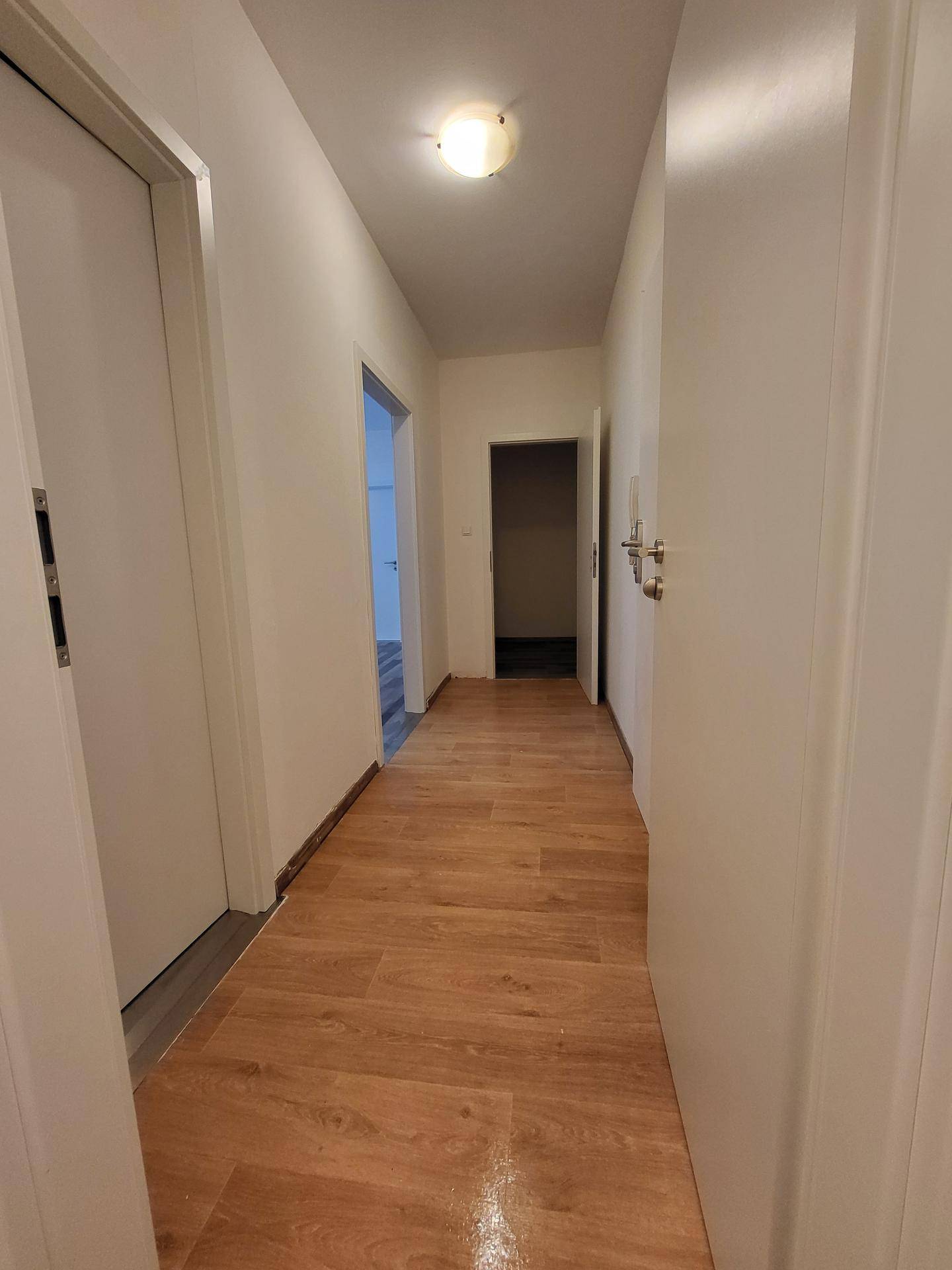 Langer, heller Flur mit Laminatboden, der verschiedene Zimmer verbindet.