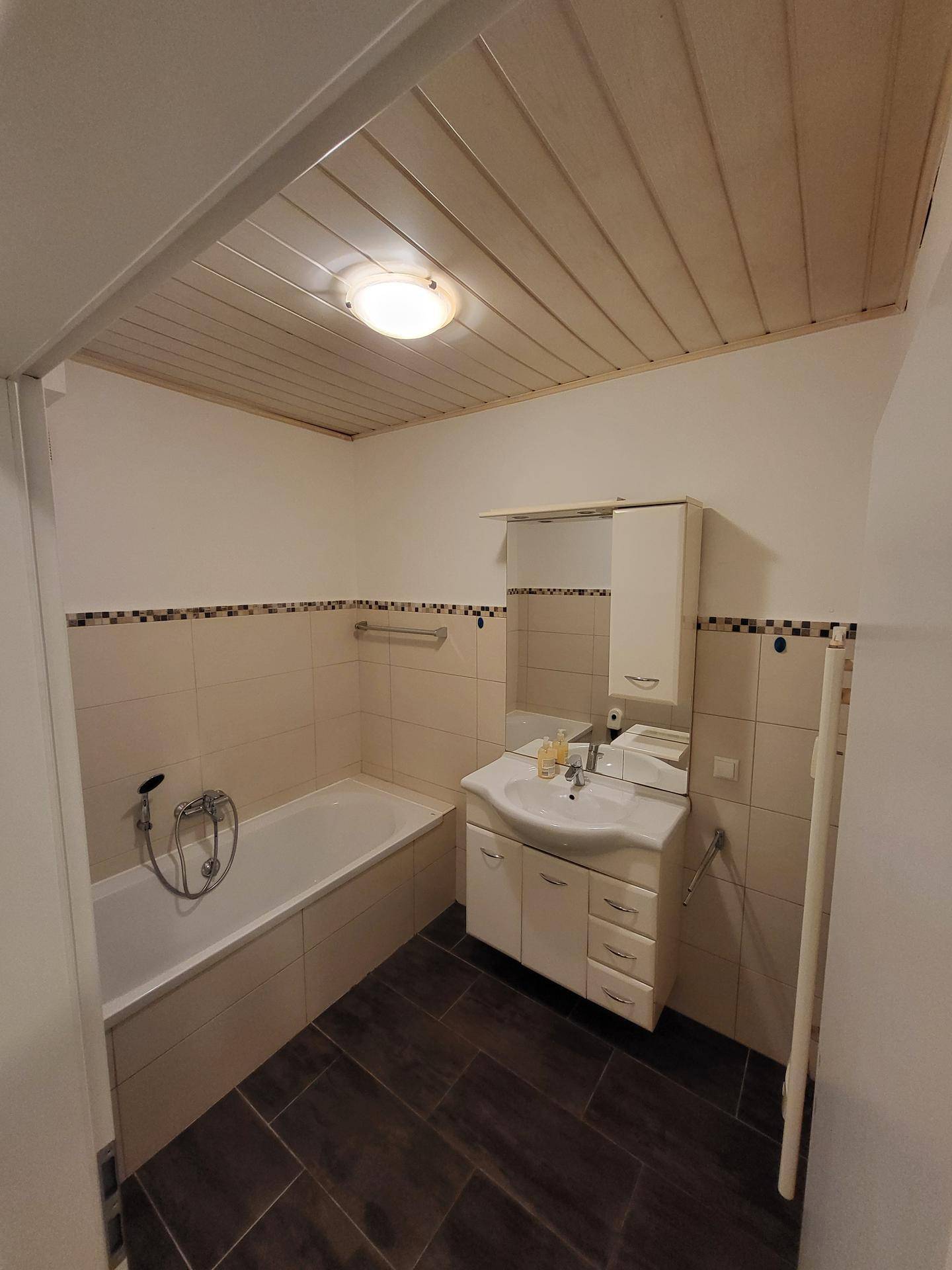 Badezimmer mit Badewanne, Waschbecken und Holzdecke, in gutem Zustand.