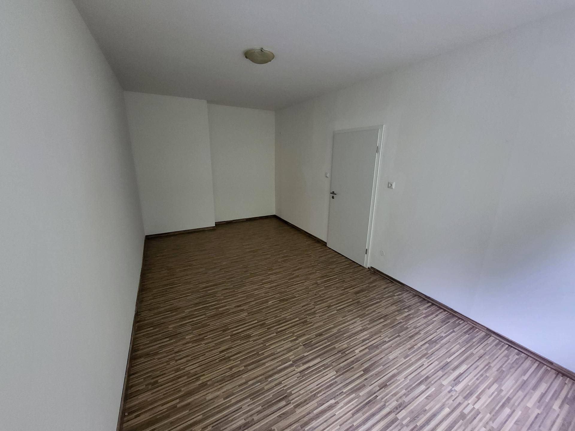 Geräumiges, leeres Zimmer mit Laminatboden und weißen Wänden.