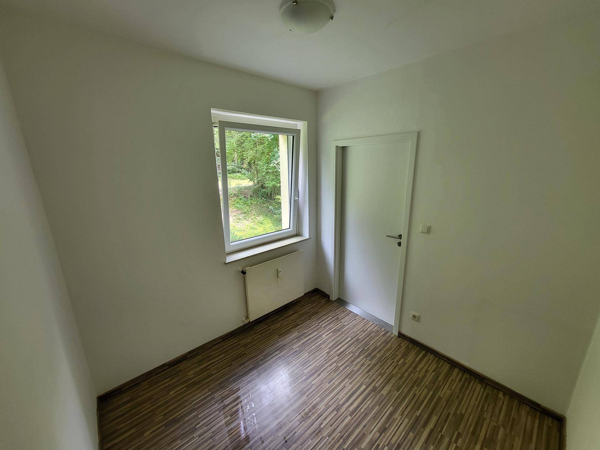 Helles Zimmer mit Laminatboden, weiß gestrichenen Wänden und Fenster.