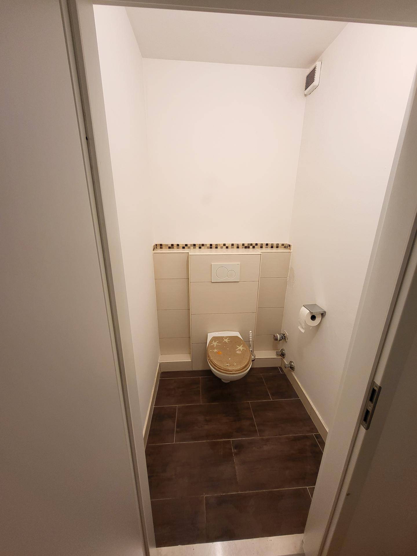 Separates WC mit Fliesenboden und Wandfliesen im unteren Bereich.