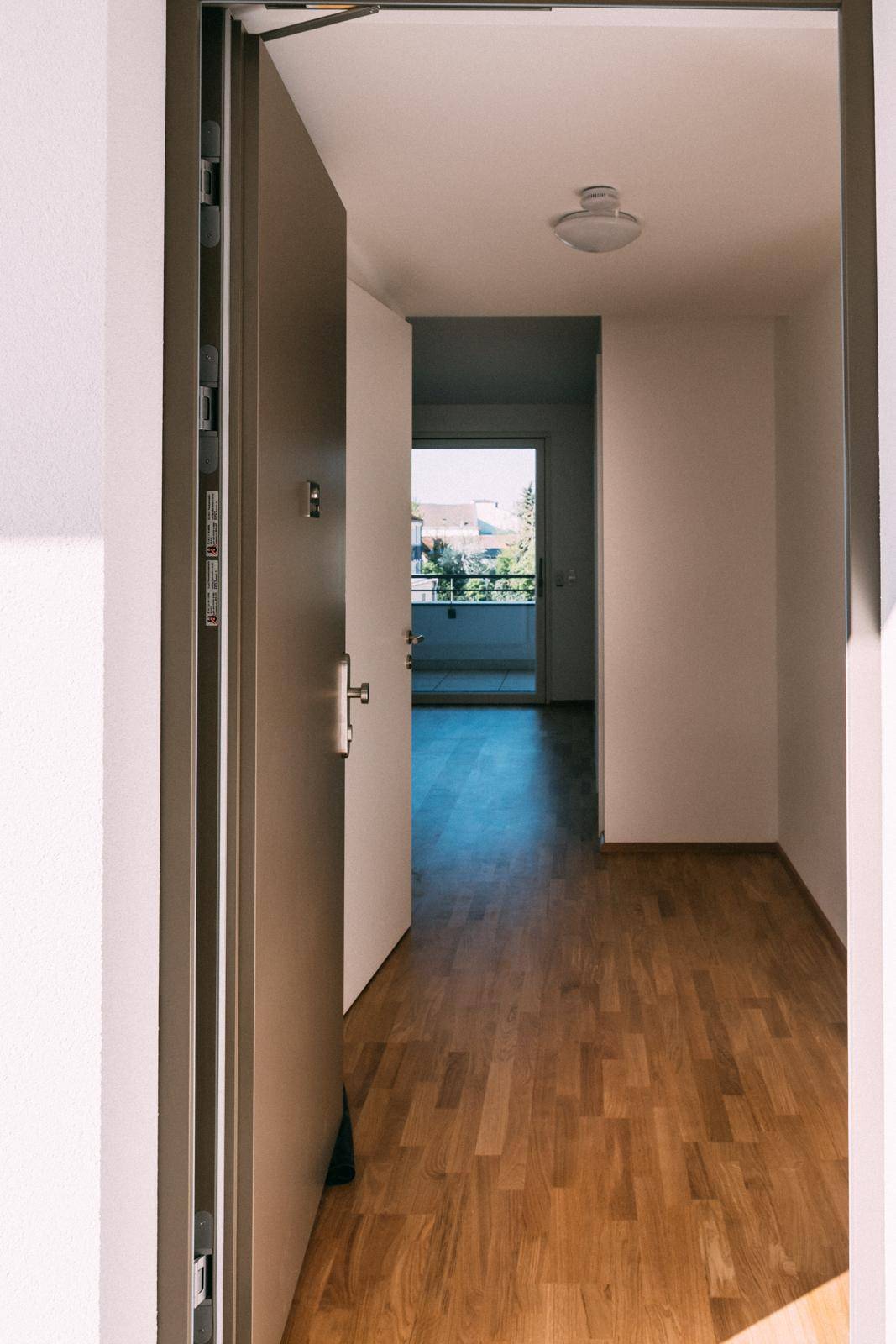 Eingangsbereich mit Holzboden und Blick durch eine offene Tür auf einen Balkon.