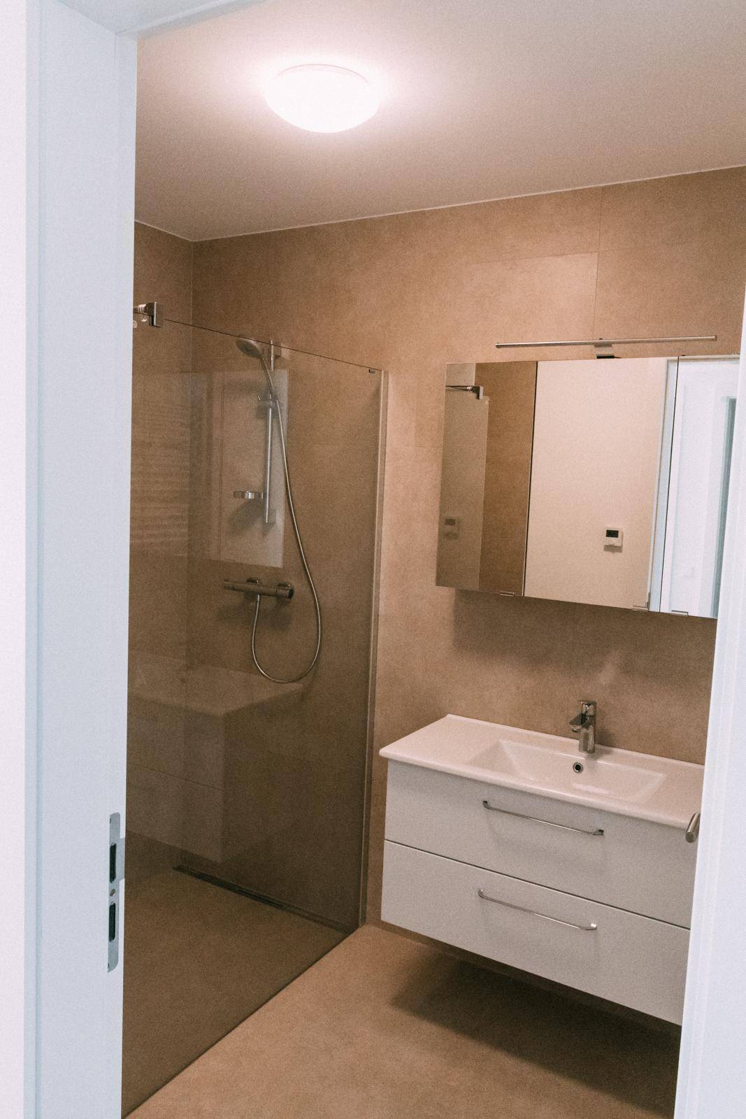 Modernes Badezimmer mit begehbarer Dusche, Waschtisch und beigefarbenen Fliesen.