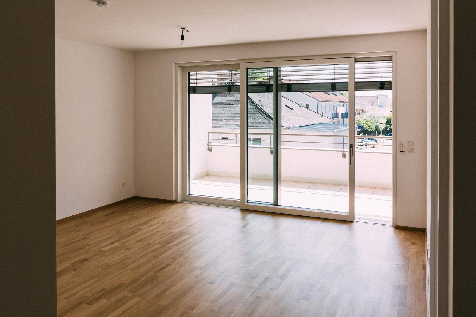 Geräumiger Wohnraum mit Holzboden und großen Schiebetüren zum Balkon.