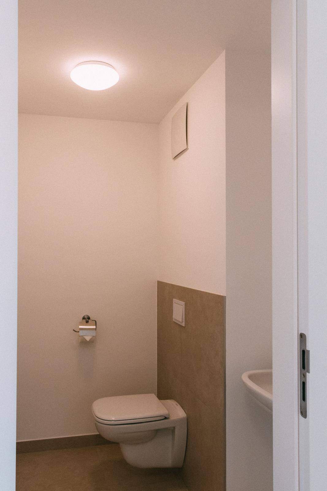 Gäste-WC mit wandhängender Toilette, kleinem Waschbecken und beigefarbenen Fliesen.