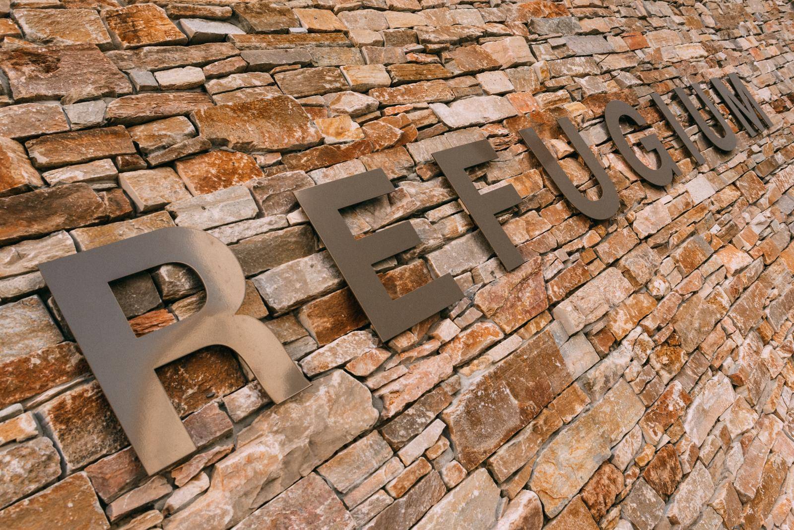 Detailaufnahme der Steinverkleidung an der Fassade mit dem Schriftzug "REFUGIUM".