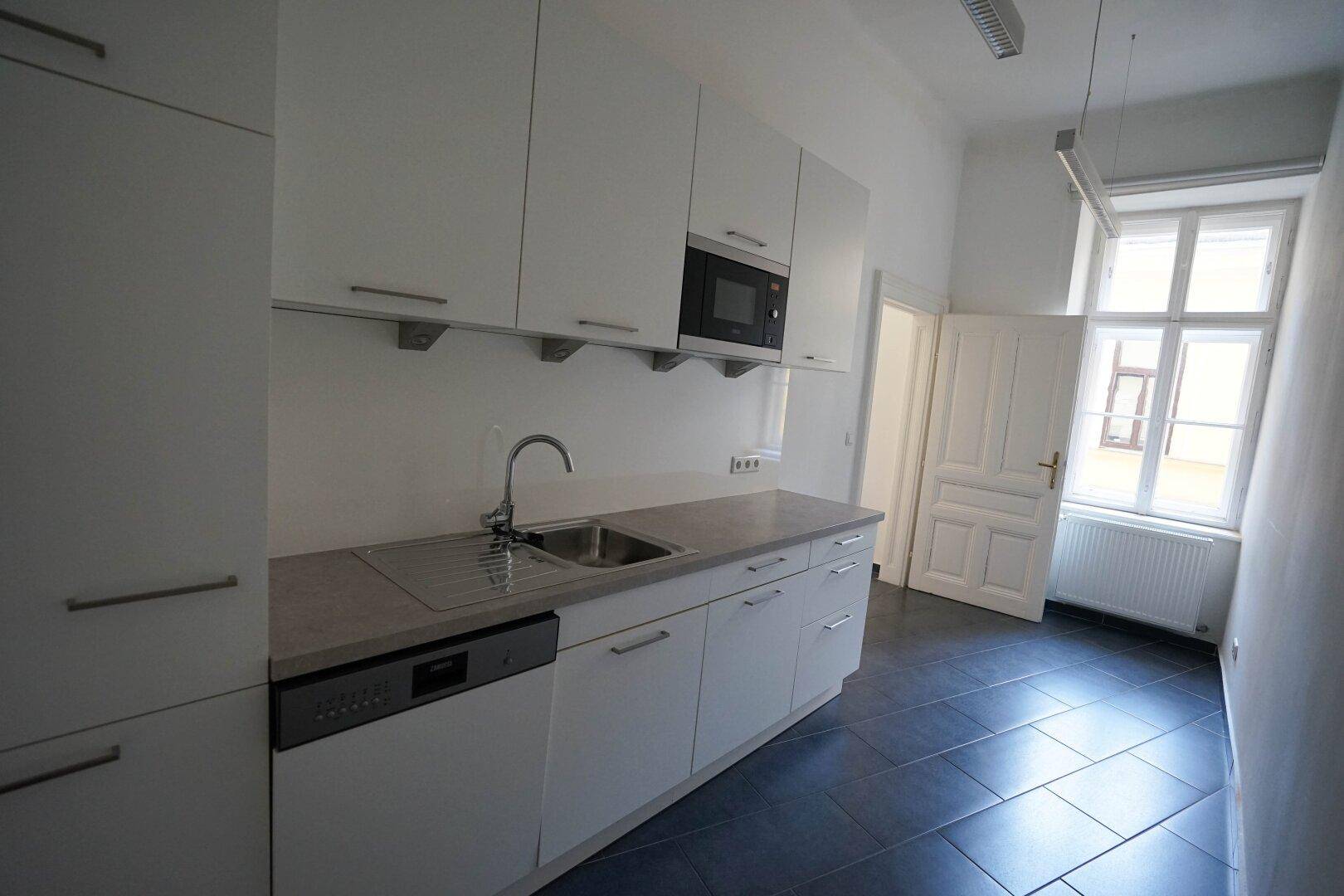 Moderne Einbauküche mit weißen Schränken, Spüle, Mikrowelle und Geschirrspüler, mit Fenster.