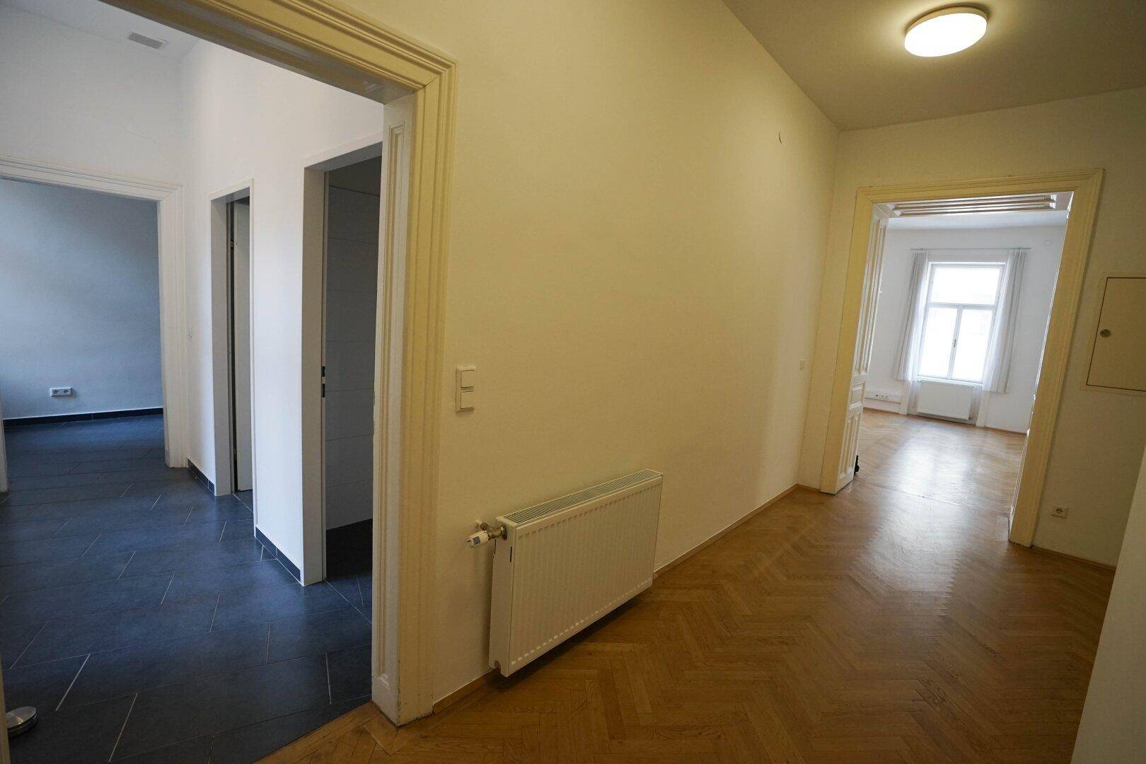 Geräumiger Flur mit Fischgrätparkett und dunklen Fliesen, der verschiedene Räume verbindet.