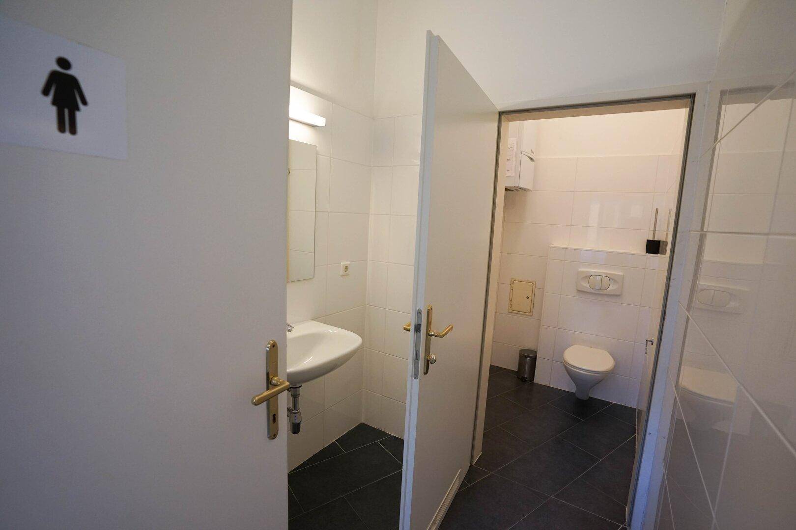 Saubere Gästetoilette mit Waschbecken, Spiegel und weiß gefliesten Wänden, gut beleuchtet.