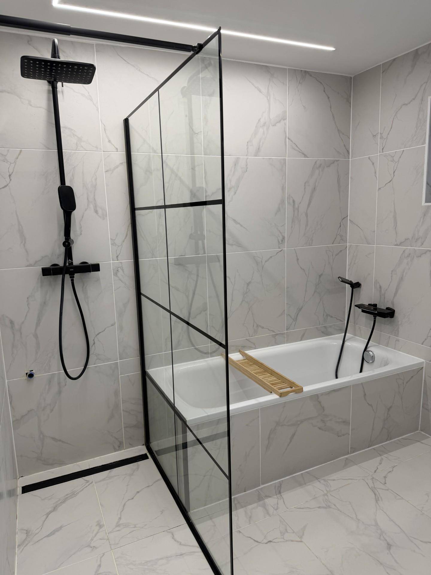 Modernes Badezimmer mit Badewanne, Duschabtrennung aus Glas und schwarzen Armaturen.