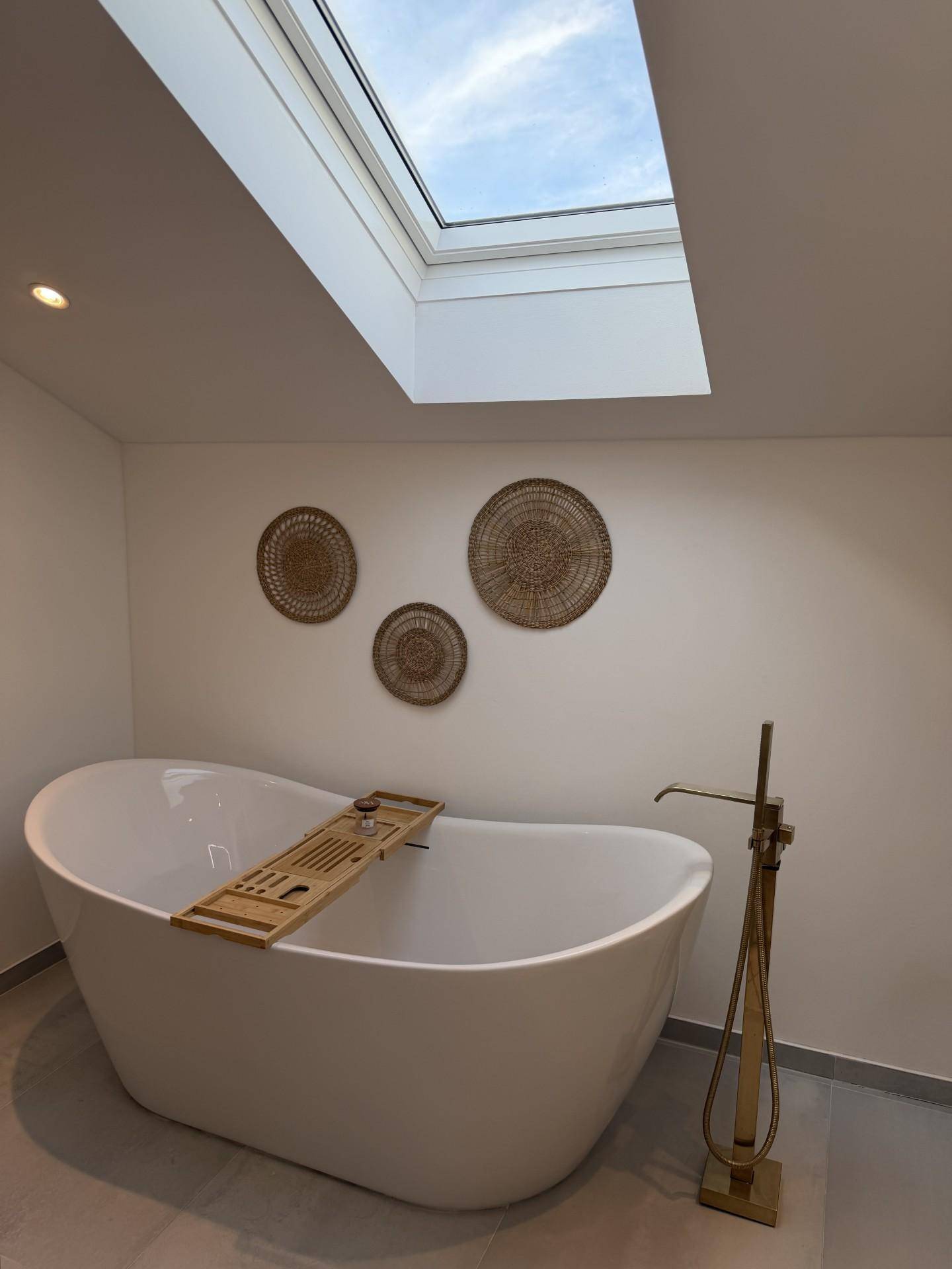 Modernes Badezimmer mit freistehender Badewanne und Dachfenster für viel Tageslicht.