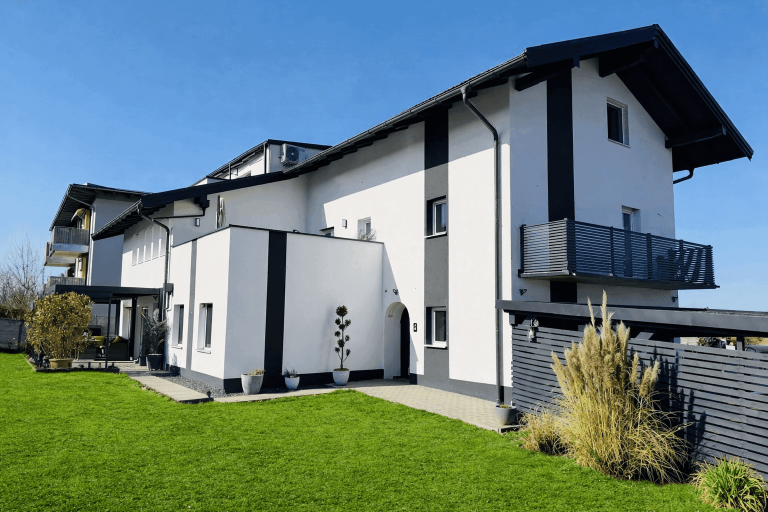 Modernes Mehrfamilienhaus mit weißer Fassade, schwarzen Akzenten und gepflegtem Vorgarten.