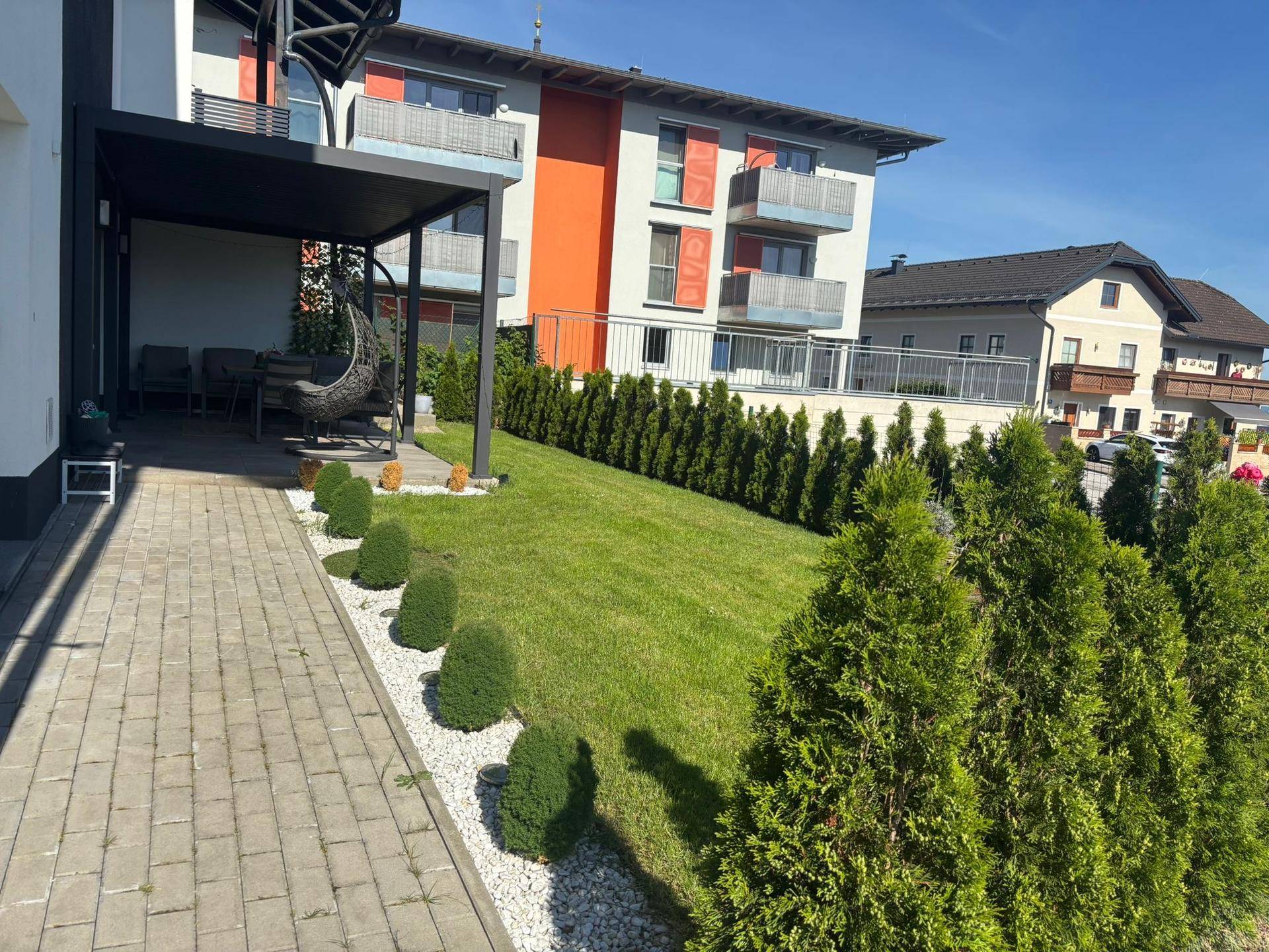 Gepflegter Gartenbereich mit Ziersträuchern, Rasenfläche und Zugang zur Terrasse.