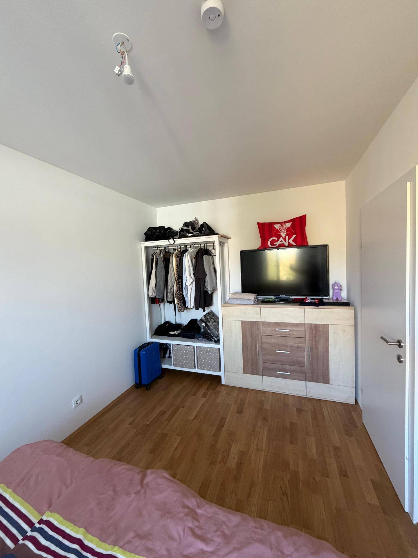 Schlafzimmer mit Holzboden, offenem Kleiderschrank und einer Kommode mit Fernseher.