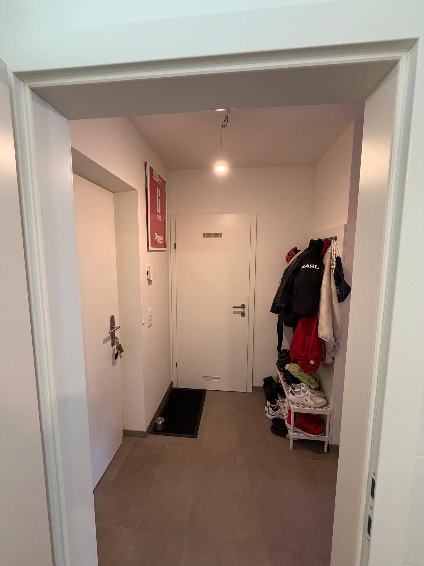 Heller Eingangsbereich mit Fliesenboden, Garderobe und einer modernen weißen Eingangstür.