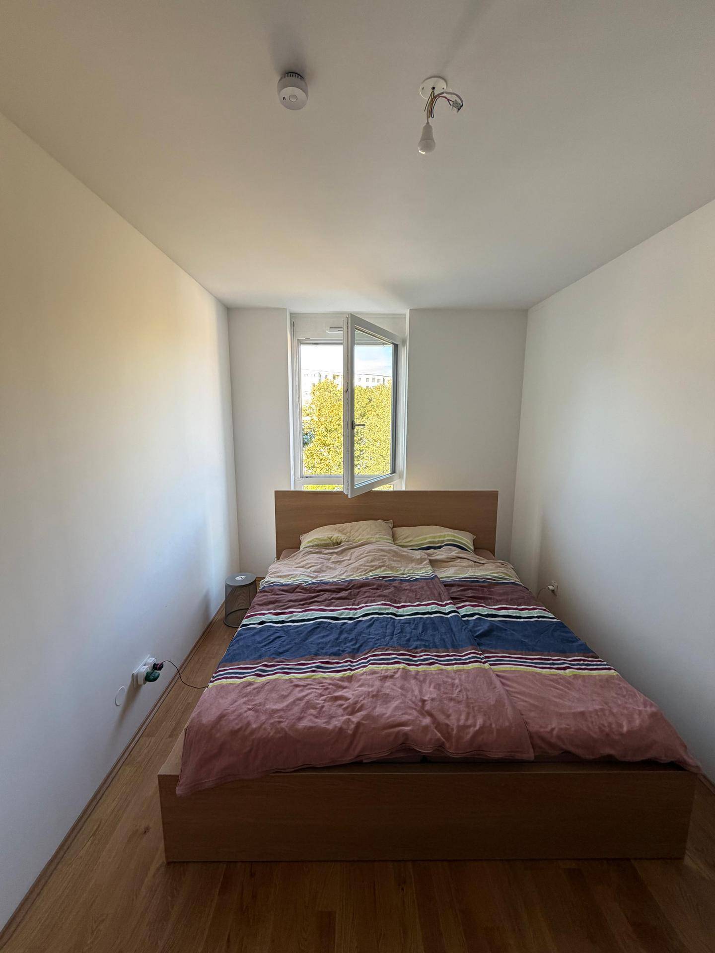 Helles Schlafzimmer mit Doppelbett, Holzboden und einem Fenster mit Blick ins Grüne.