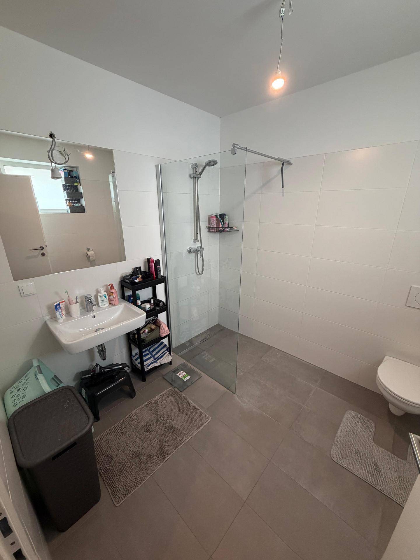 Modernes Badezimmer mit ebenerdiger Dusche, Waschbecken, WC und hellen Fliesen.