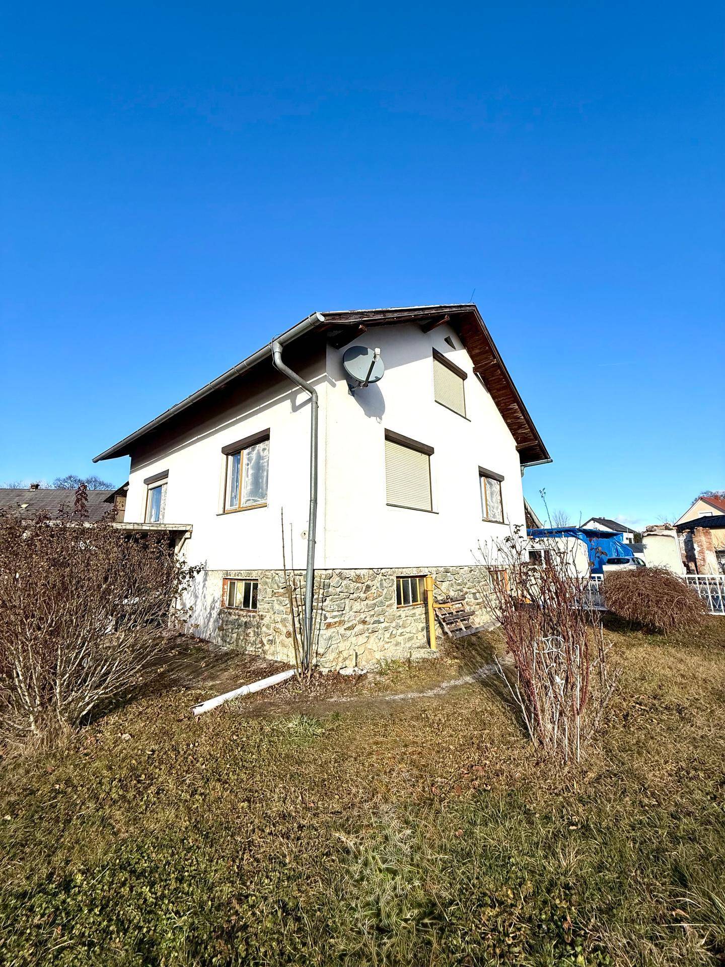 Einfamilienhaus mit Steinsockel und Rollläden, umgeben von einem großen, naturbelassenen Garten.