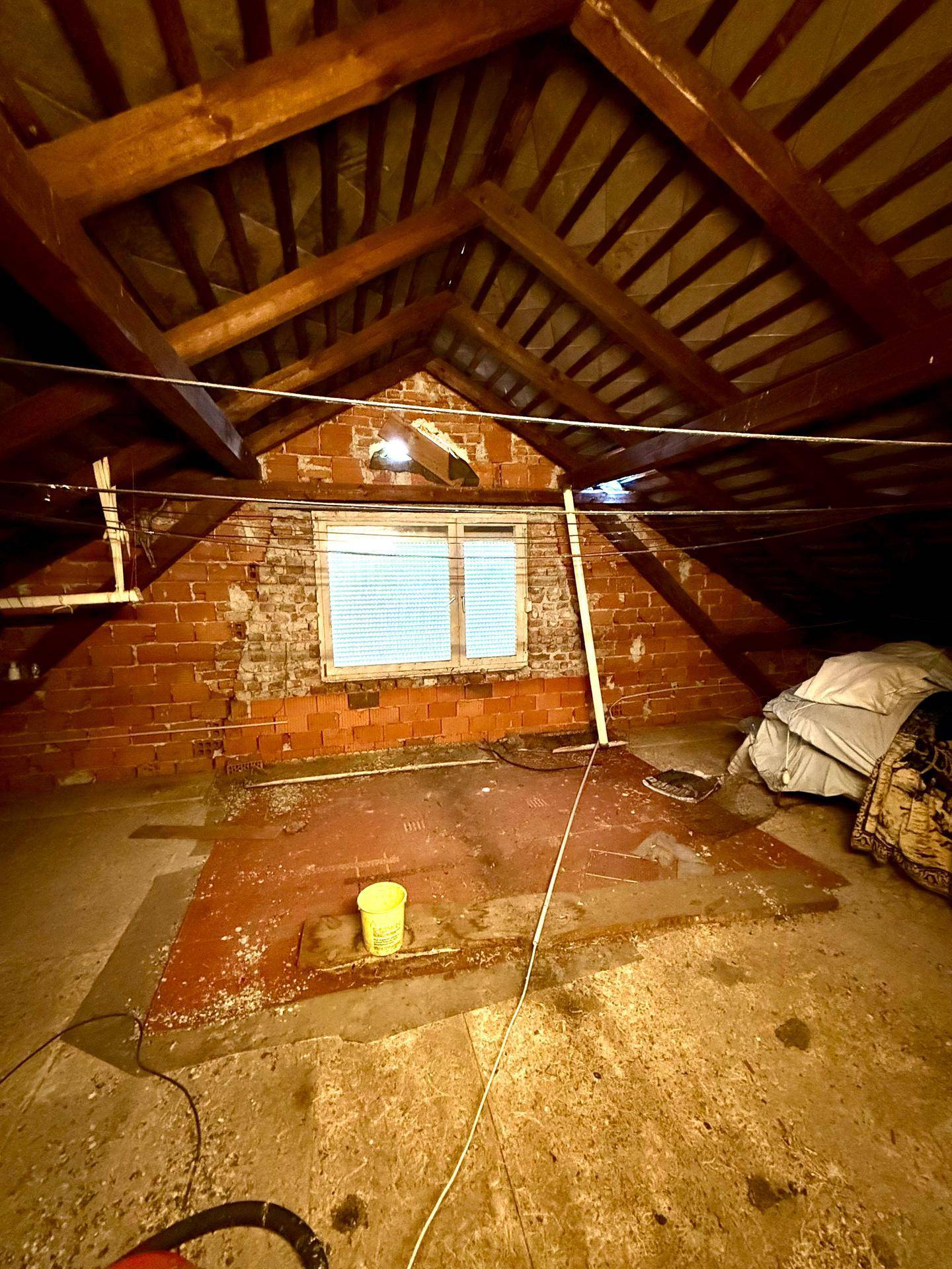 Unausgebauter Dachboden mit sichtbaren Holzbalken und Ziegelwänden, bietet Ausbaupotenzial.