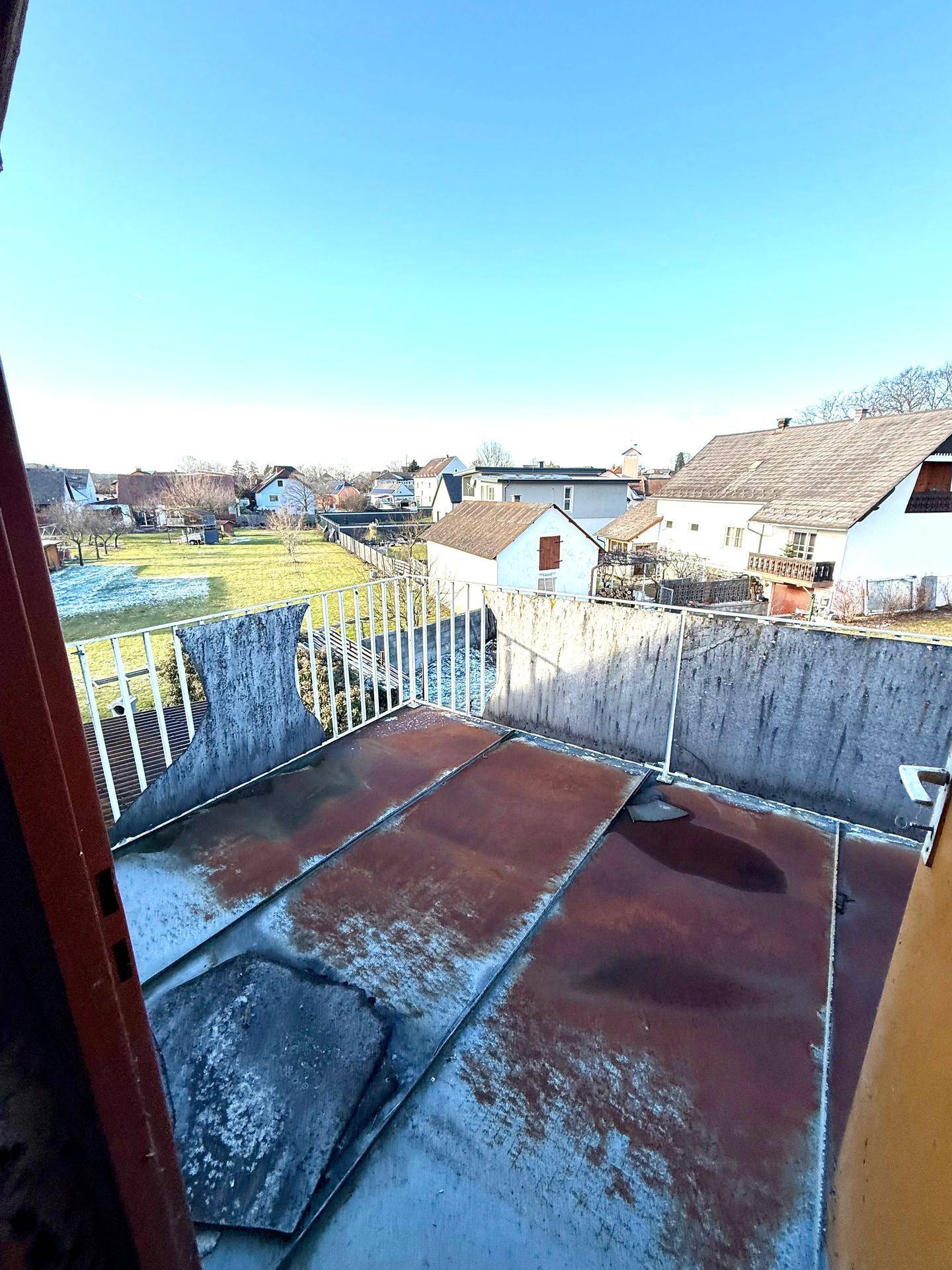 Balkon mit rostigen Metallplatten und Blick auf die Umgebung, renovierungsbedürftig.