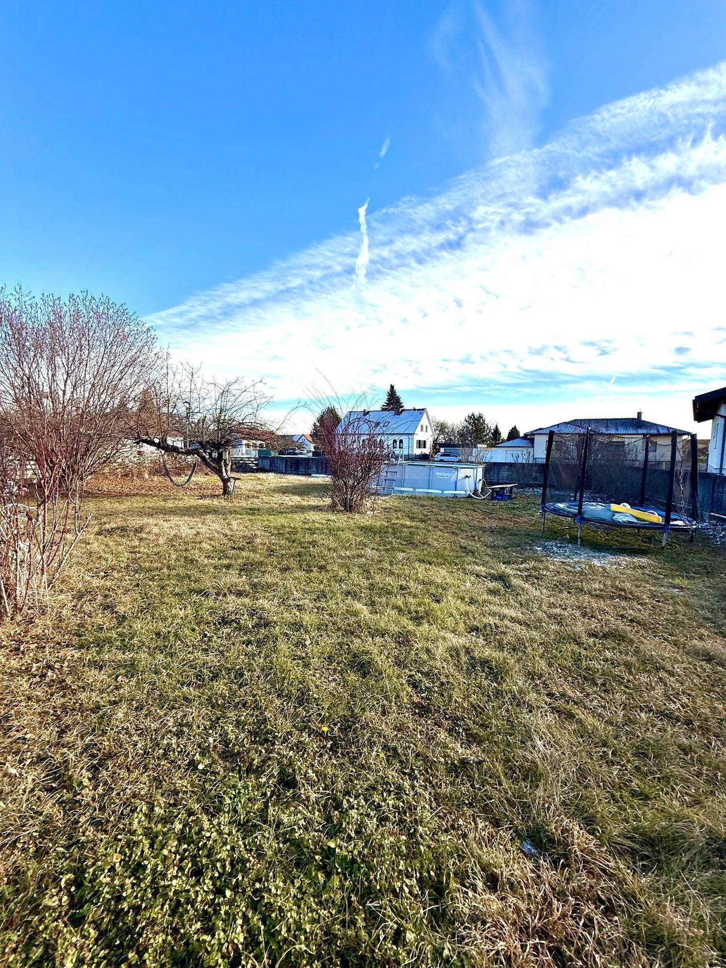 Großer Garten mit Trampolin und Aufstellpool, umgeben von Bäumen und Grünflächen.