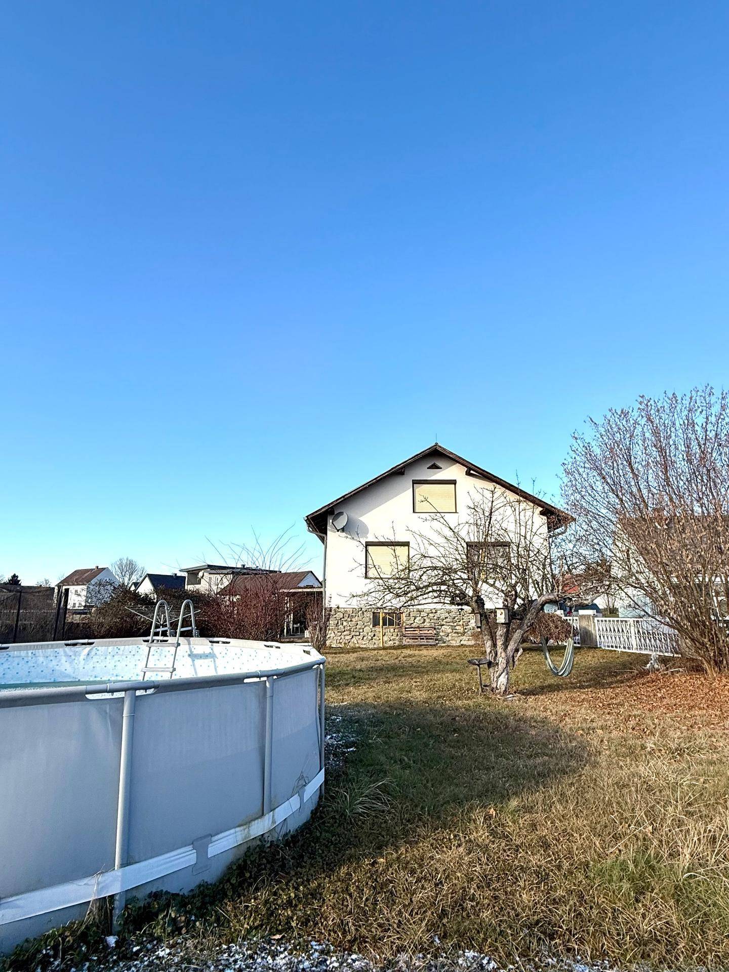 Einfamilienhaus mit Garten und Aufstellpool, umgeben von Bäumen und Grünflächen.