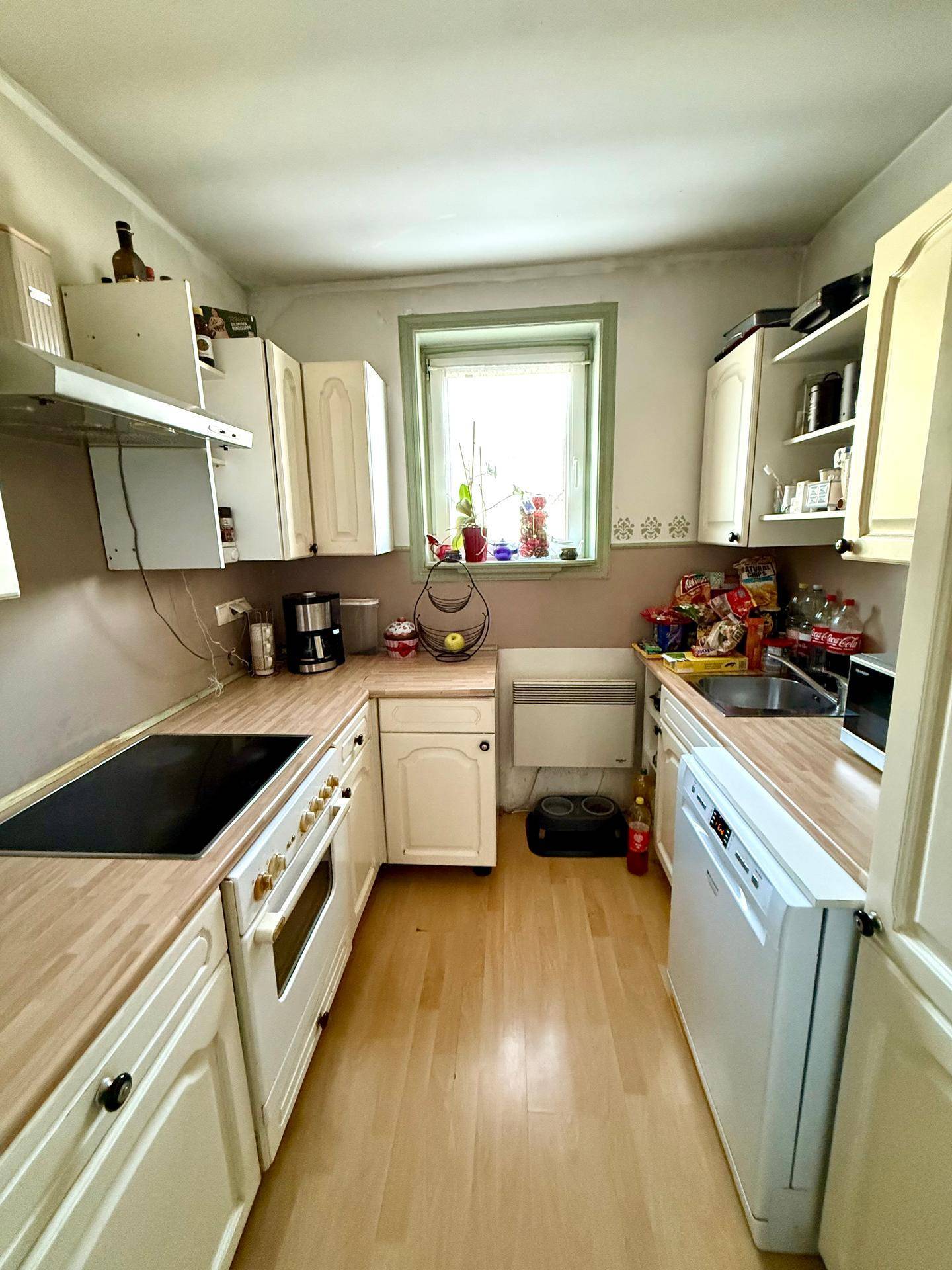 Ältere Küche mit weißen Schränken, Holzarbeitsplatten und Holzboden, funktional eingerichtet.