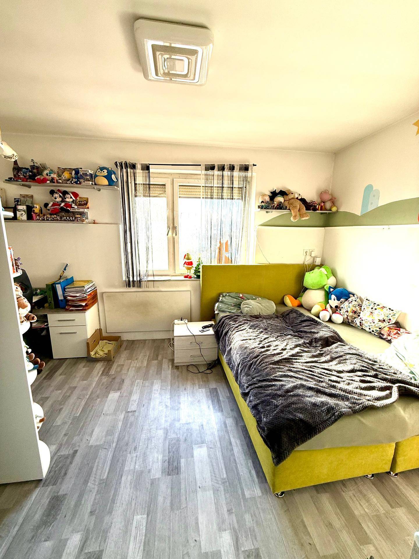 Kinderzimmer mit Einzelbett, Schreibtisch und Laminatboden, hell und funktional eingerichtet.