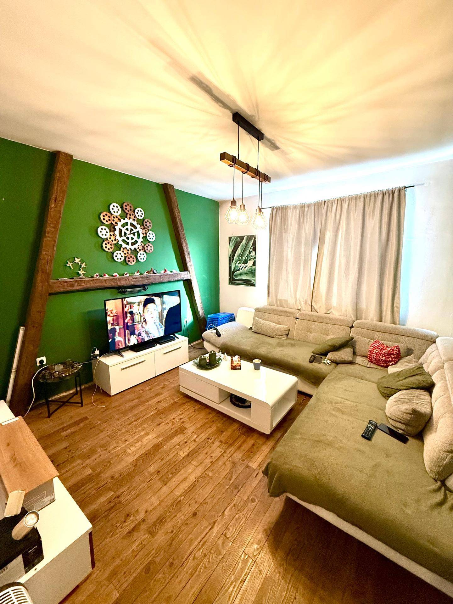 Wohnzimmer mit grün gestrichenen Wänden, Holzbalken und Sofa, gemütlich eingerichtet.